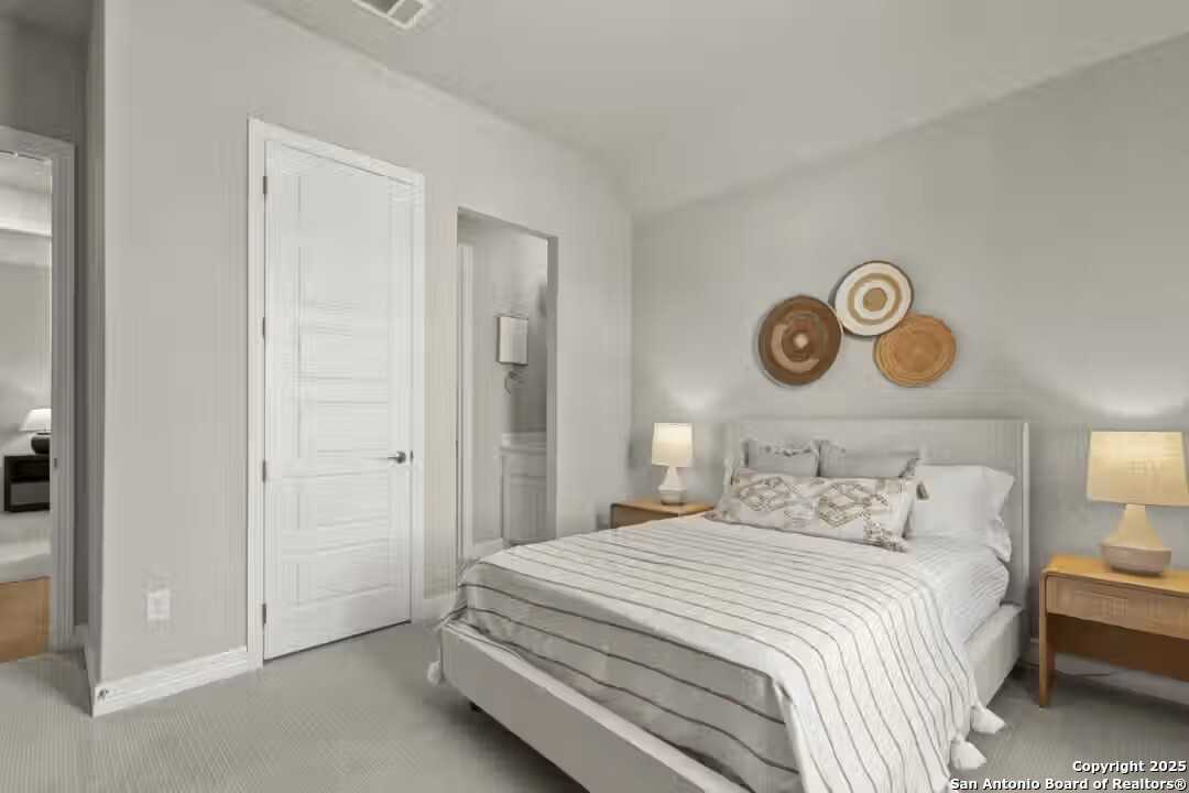 Cozy bedroom with light gray walls, striped bedding, woven wall art, and en-suite door in Davidson Homes The Summerlin B, Castroville, Texas