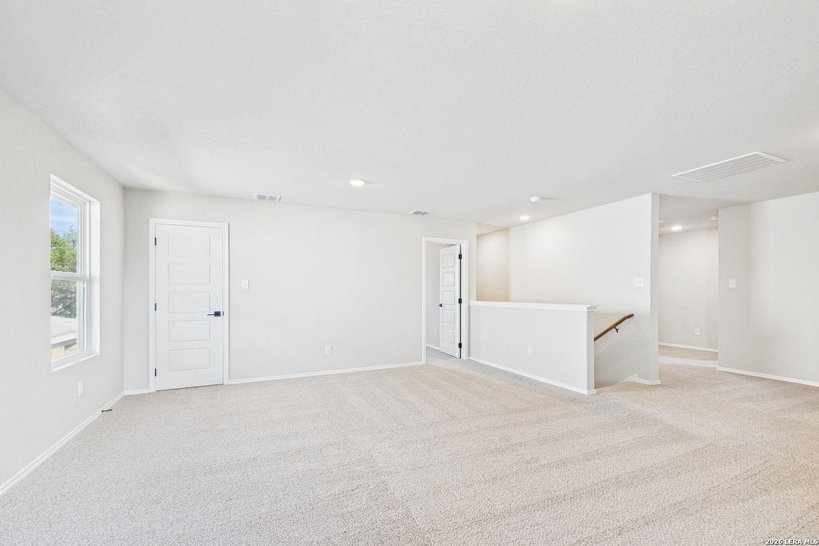 Spacious upstairs loft with beige carpet, white walls, large windows, and staircase railing in Davidson Homes The Douglas E, San Antonio