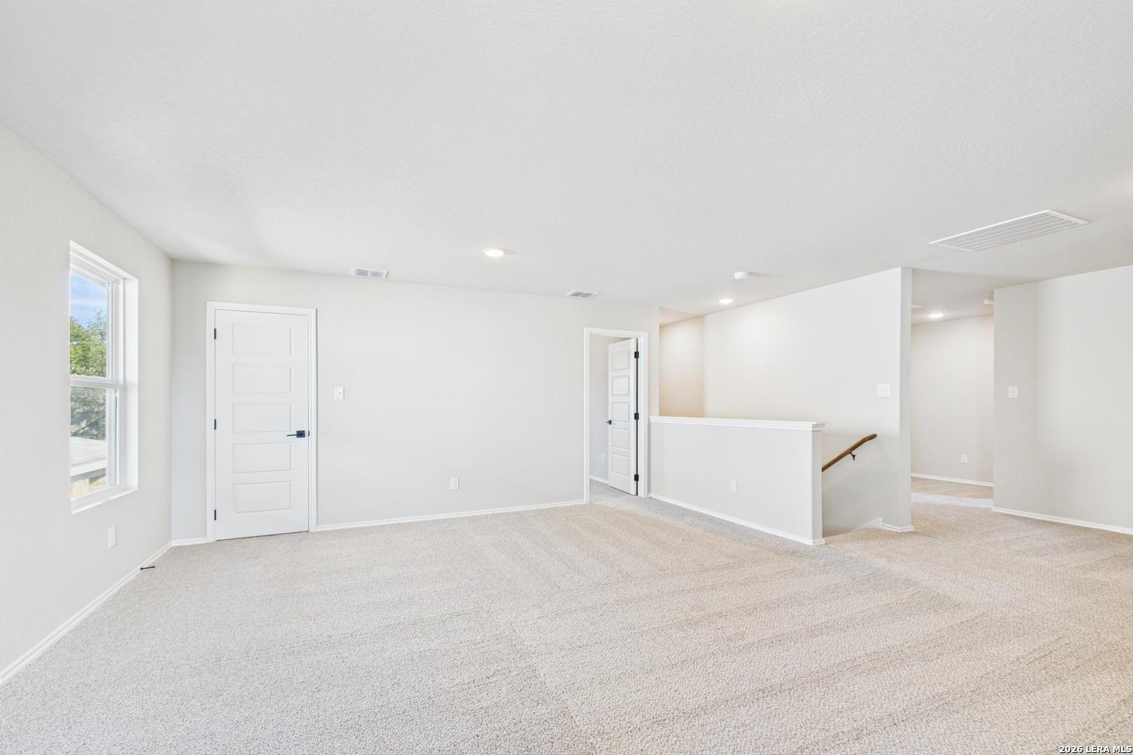 Spacious upstairs loft with beige carpet, white walls, large windows, and staircase railing in Davidson Homes The Douglas E, San Antonio