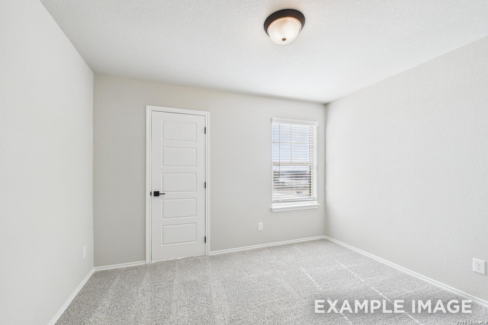 Bright, carpeted bedroom with neutral walls and a closet door in The Charlotte B floor plan at Cedar Heights, San Antonio.