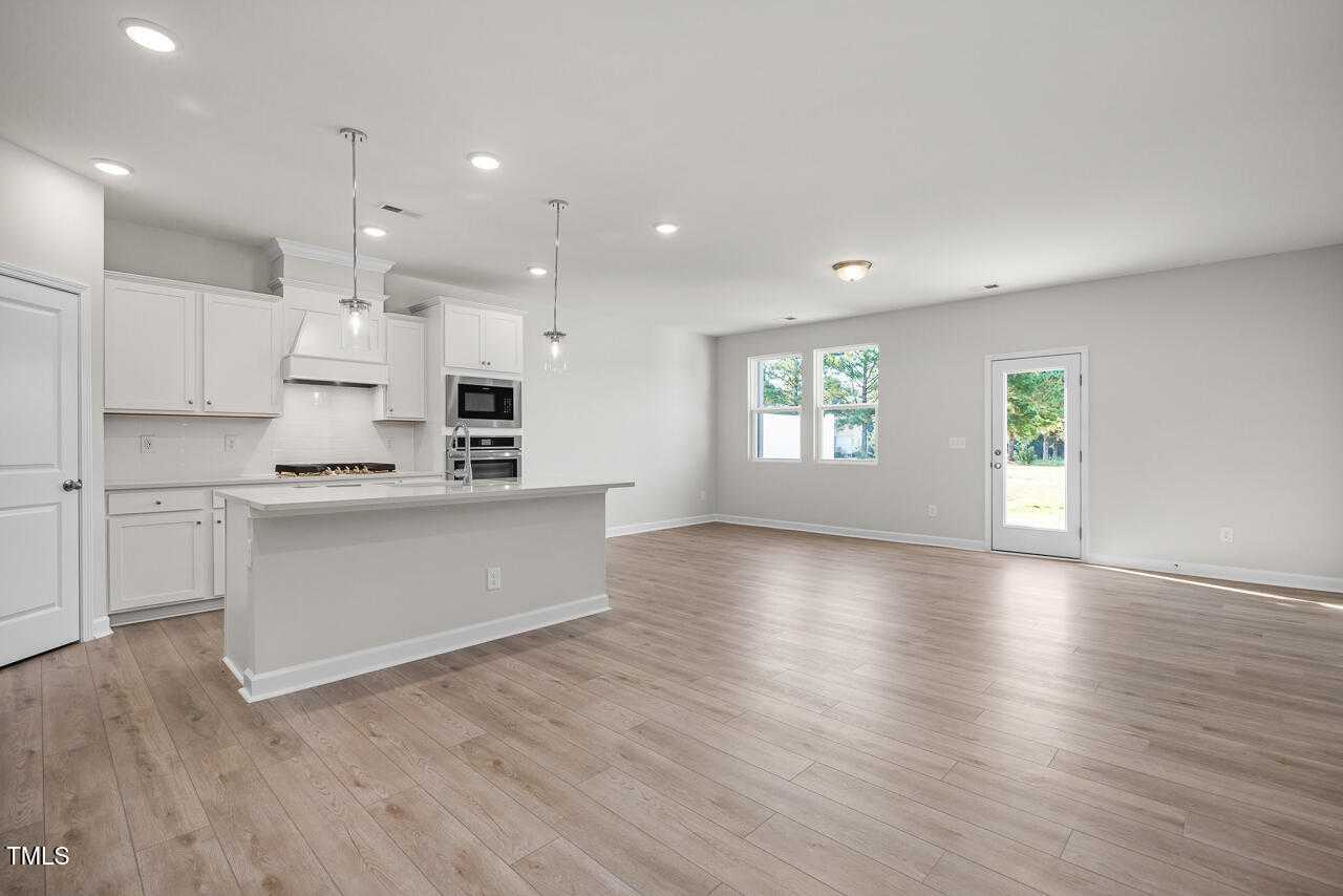 Modern open-concept kitchen with white cabinets, stainless appliances, and large island in Davidson Homes The Warren, Fuquay-Varina, NC