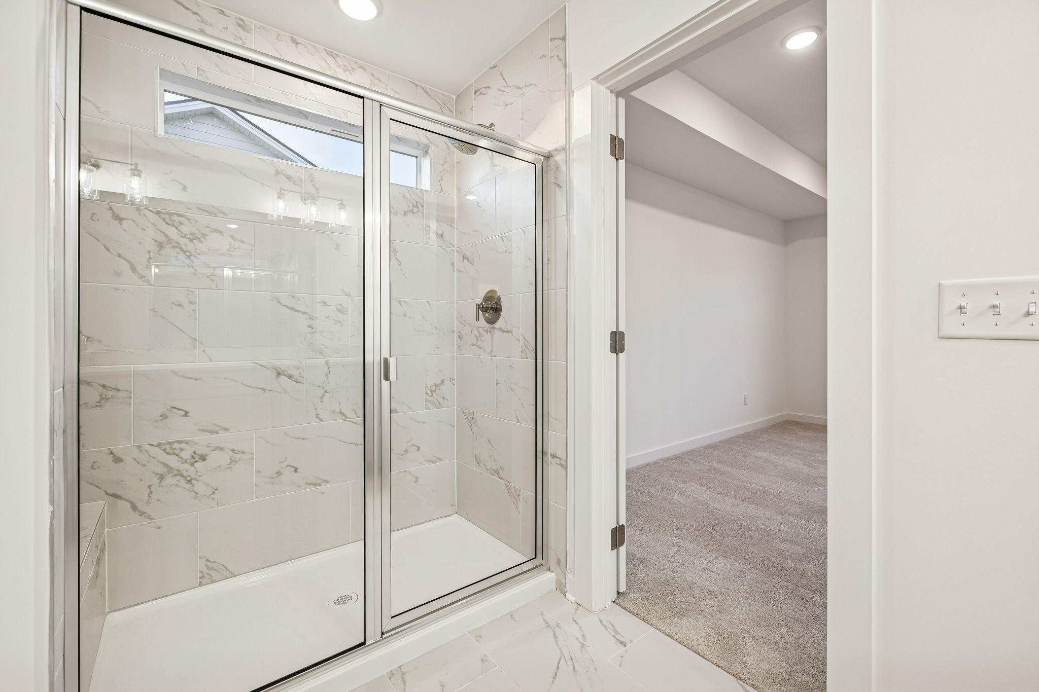 Elegant walk-in shower with white marble tiles, glass enclosure, and bench in master bath, Davidson Homes The Willow, White House TN