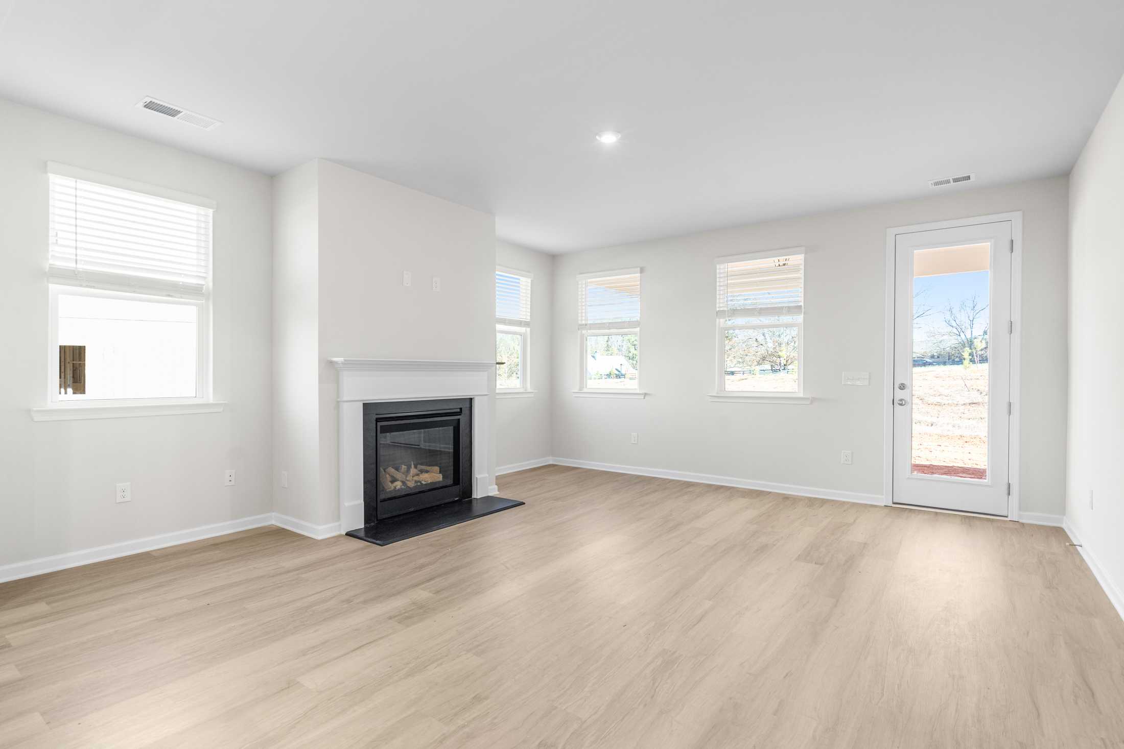 Spacious open living room in The Glenwood A featuring modern gas fireplace, light wood floors, and large windows