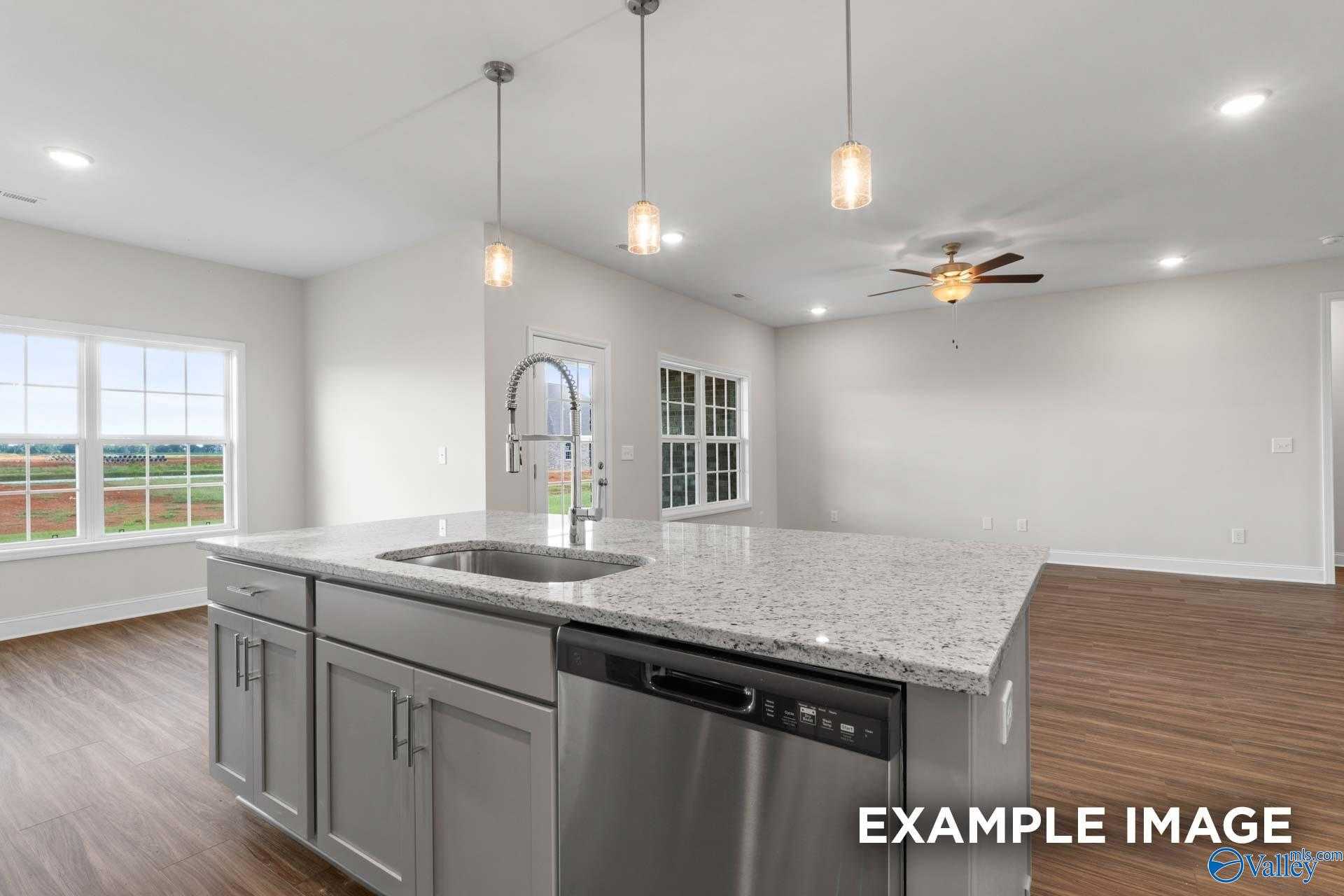 Modern open-concept kitchen with granite island, stainless sink, dishwasher, and pendant lights in The Montgomery floor plan, Hartselle, Alabama
