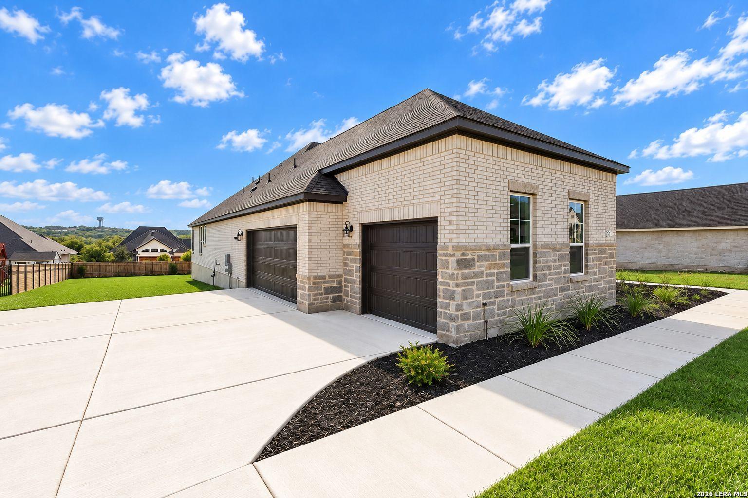 Brick and stone exterior with 3-car garage and wide driveway at Davidson Homes The Foster E in Potranco Oaks, Castroville, Texas