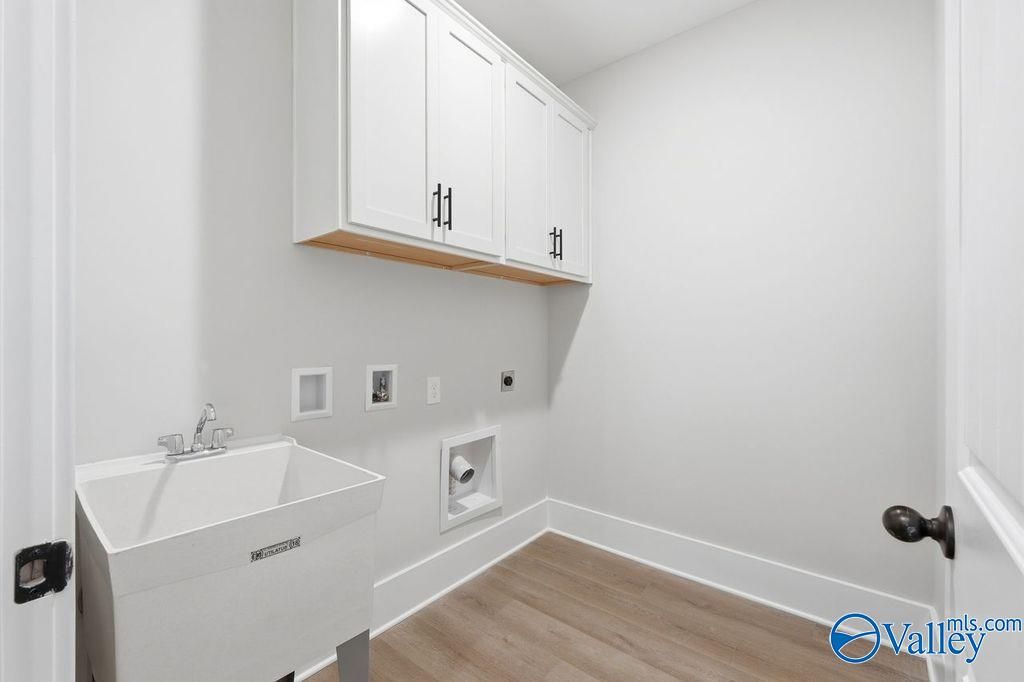 Bright laundry room featuring white cabinets, utility sink, and hardwood floors in Davidson Homes The Rockford, Hartselle, AL