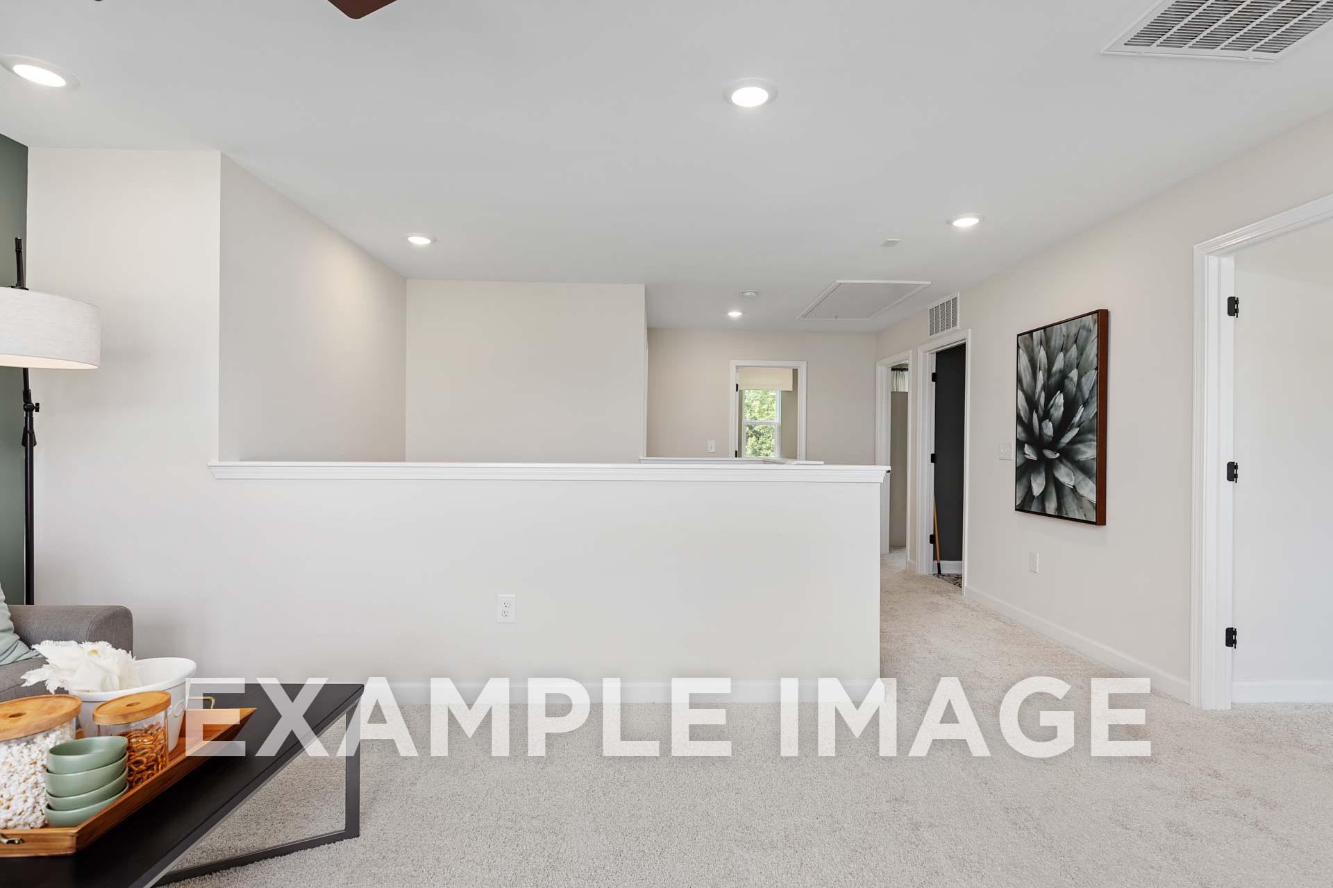 Spacious upper floor of The Willow E showcasing neutral beige walls, recessed lighting, abstract black art, and cozy gray seating