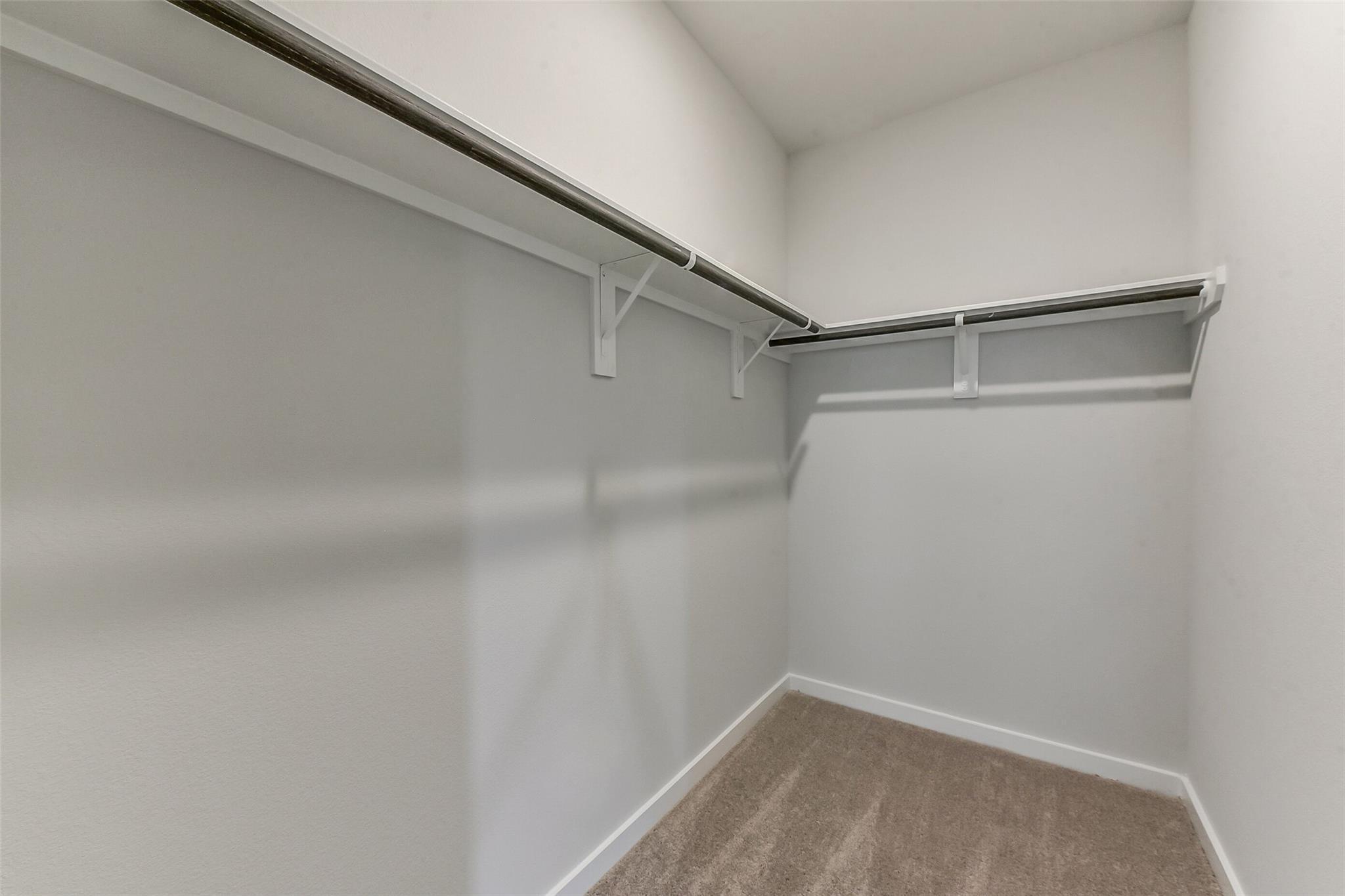 Spacious walk-in closet with white shelving, metal rods, and beige carpet in Davidson Homes The Sabine F, Dayton, Texas