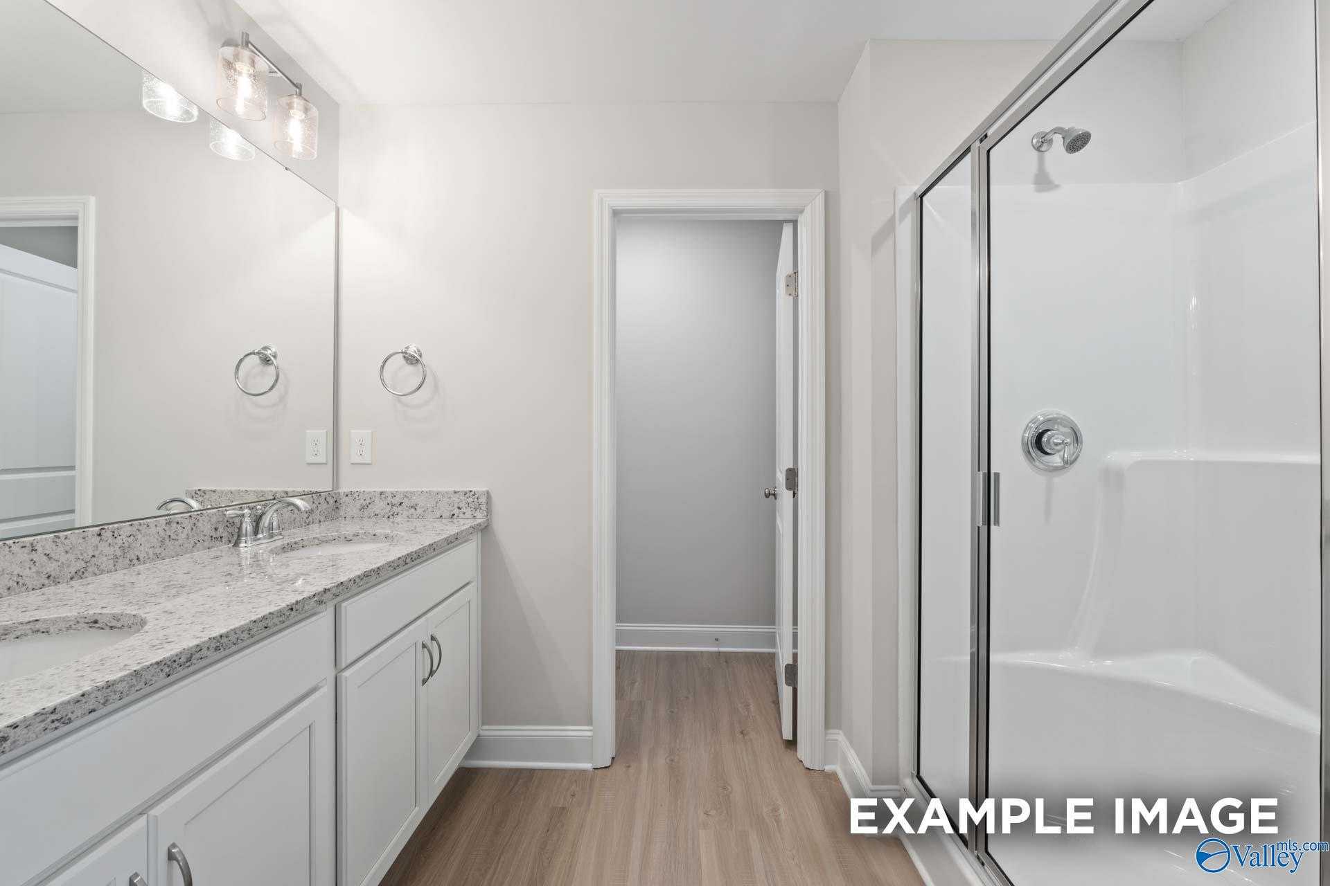 Modern master bathroom featuring double vanity with quartz counters, frameless glass shower, and walk-in closet access in Davidson Homes The Camden C, Huntsville