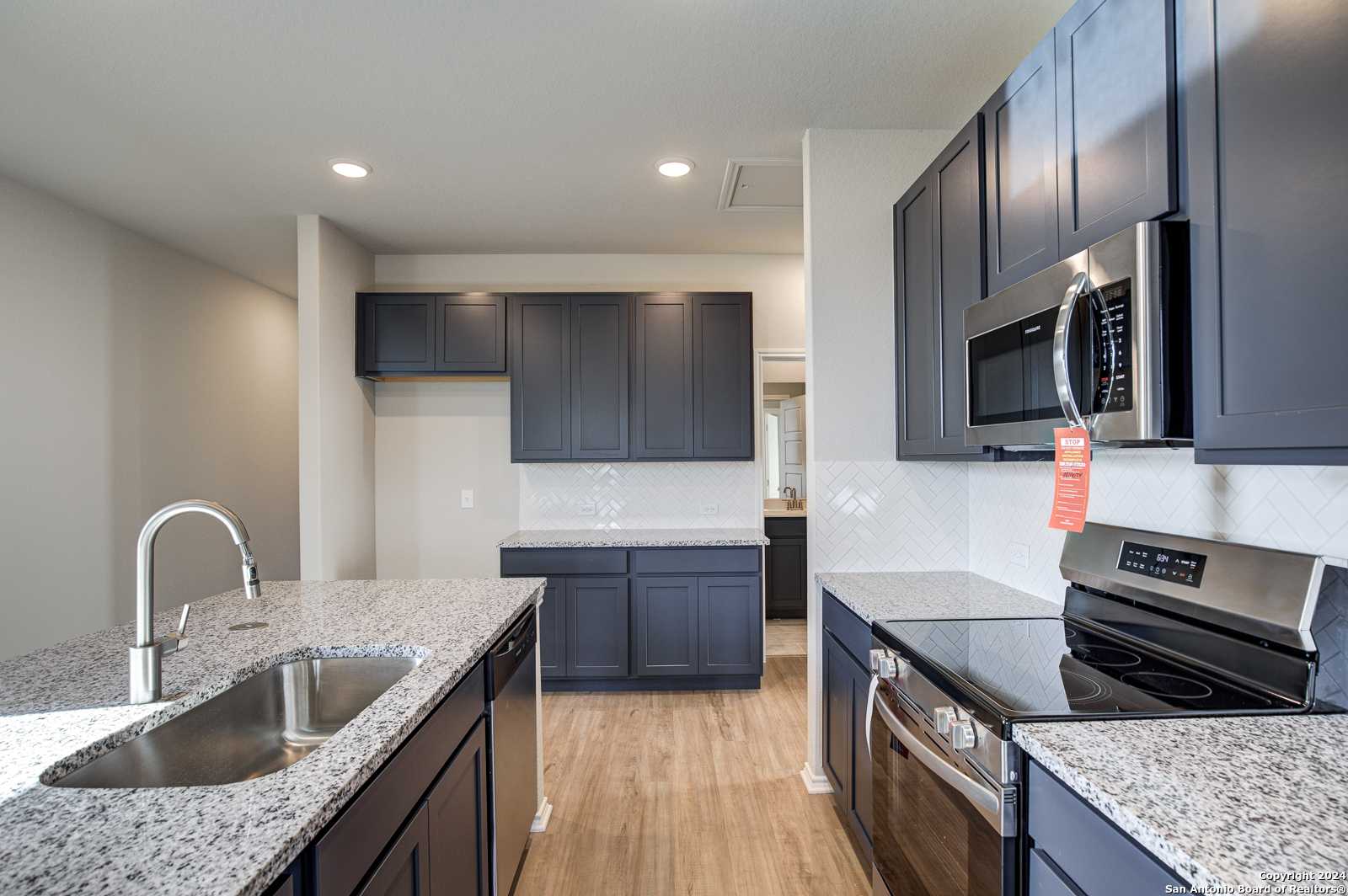 Modern kitchen with granite countertops, stainless steel appliances, and dark gray cabinets in Davidson Homes The Frio B, San Antonio