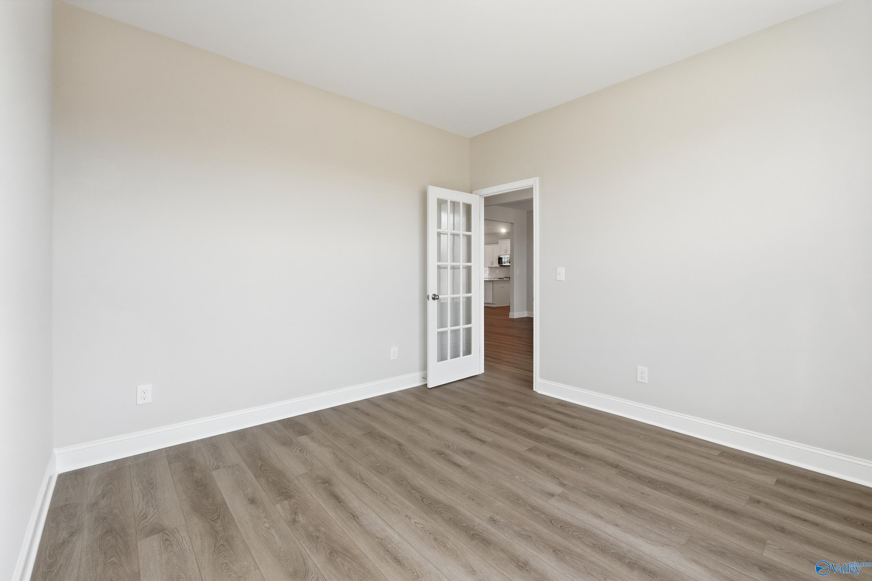 Bright empty bedroom with beige walls, luxury vinyl plank floors, and glass-paneled French door in The Finleigh plan, Harvest, Alabama