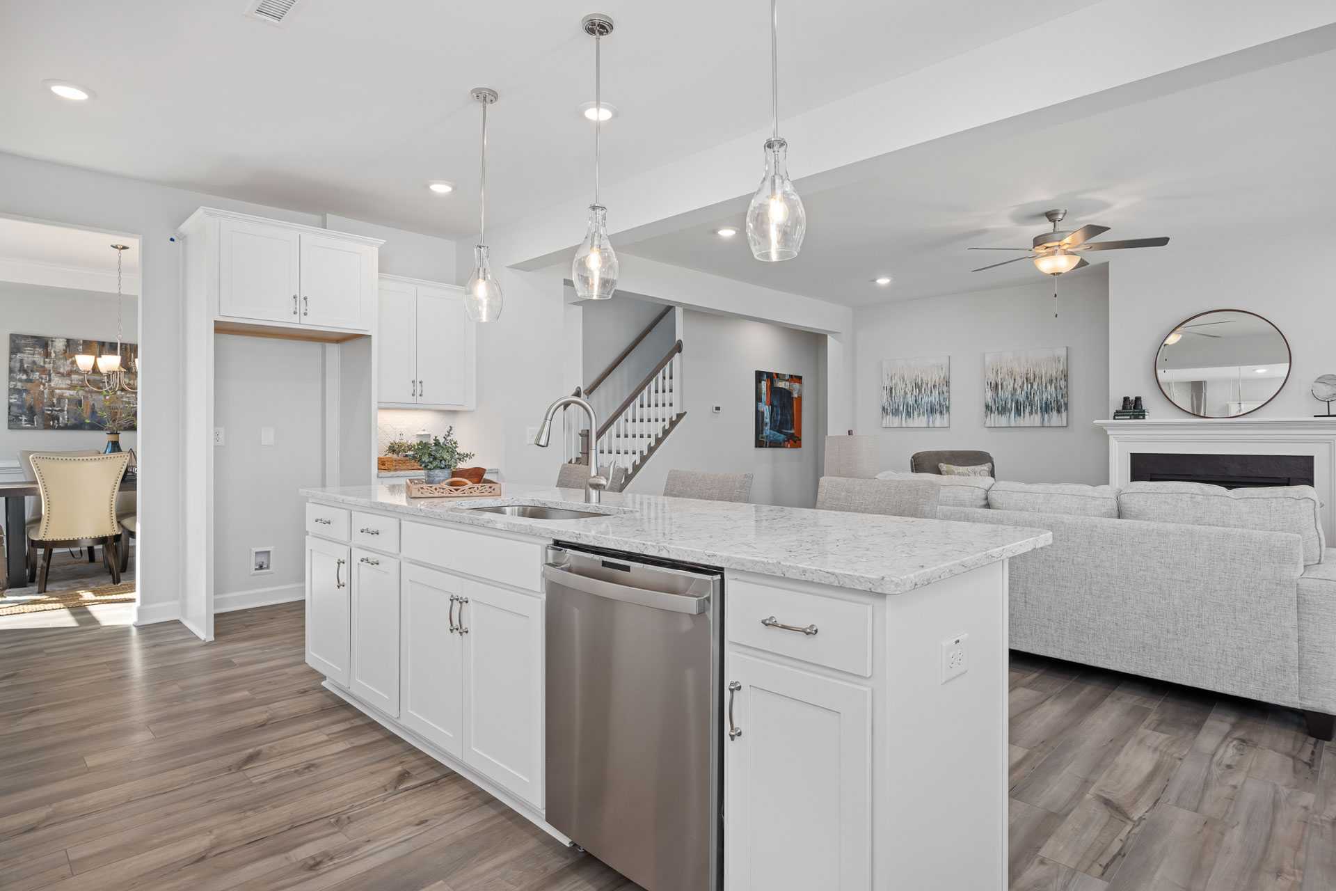 Open-concept kitchen and living room at Bentwinds in Fuquay-Varina NC with white cabinets, quartz island, stainless appliances, hardwood floors