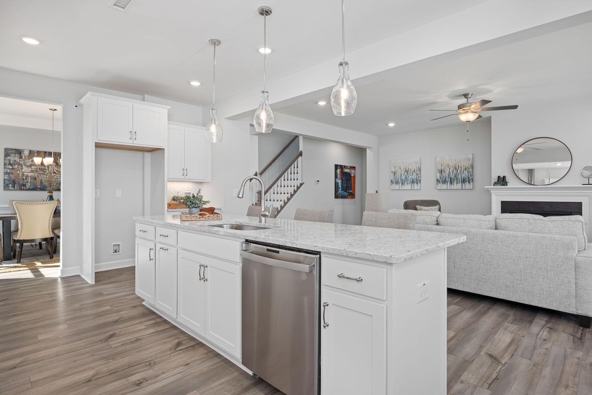 Open-concept kitchen and living room at Bentwinds in Fuquay-Varina NC with white cabinets, quartz island, stainless appliances, hardwood floors