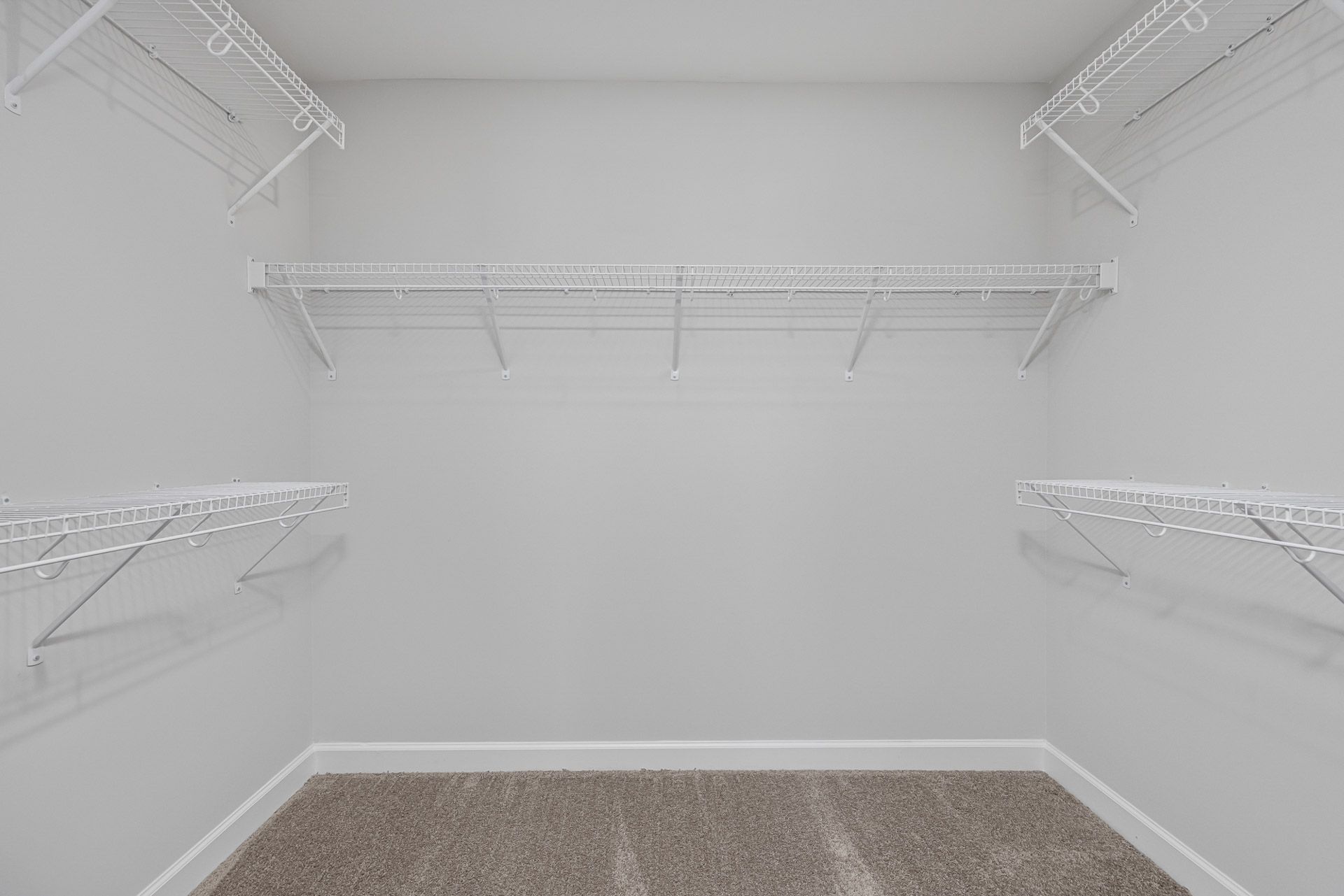 Walk-in closet with white wire shelving at Gregory Village in Lillington, NC by Davidson Homes with plush carpet flooring.