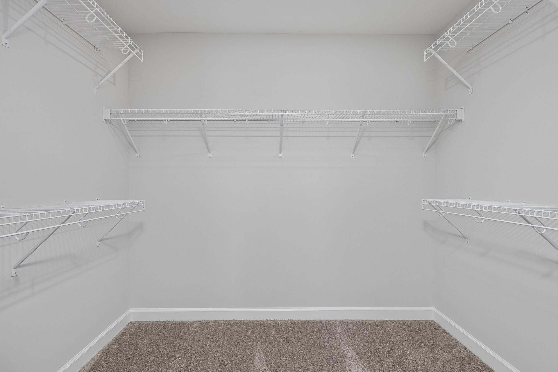 Walk-in closet with white wire shelving at Gregory Village in Lillington, NC by Davidson Homes with plush carpet flooring.