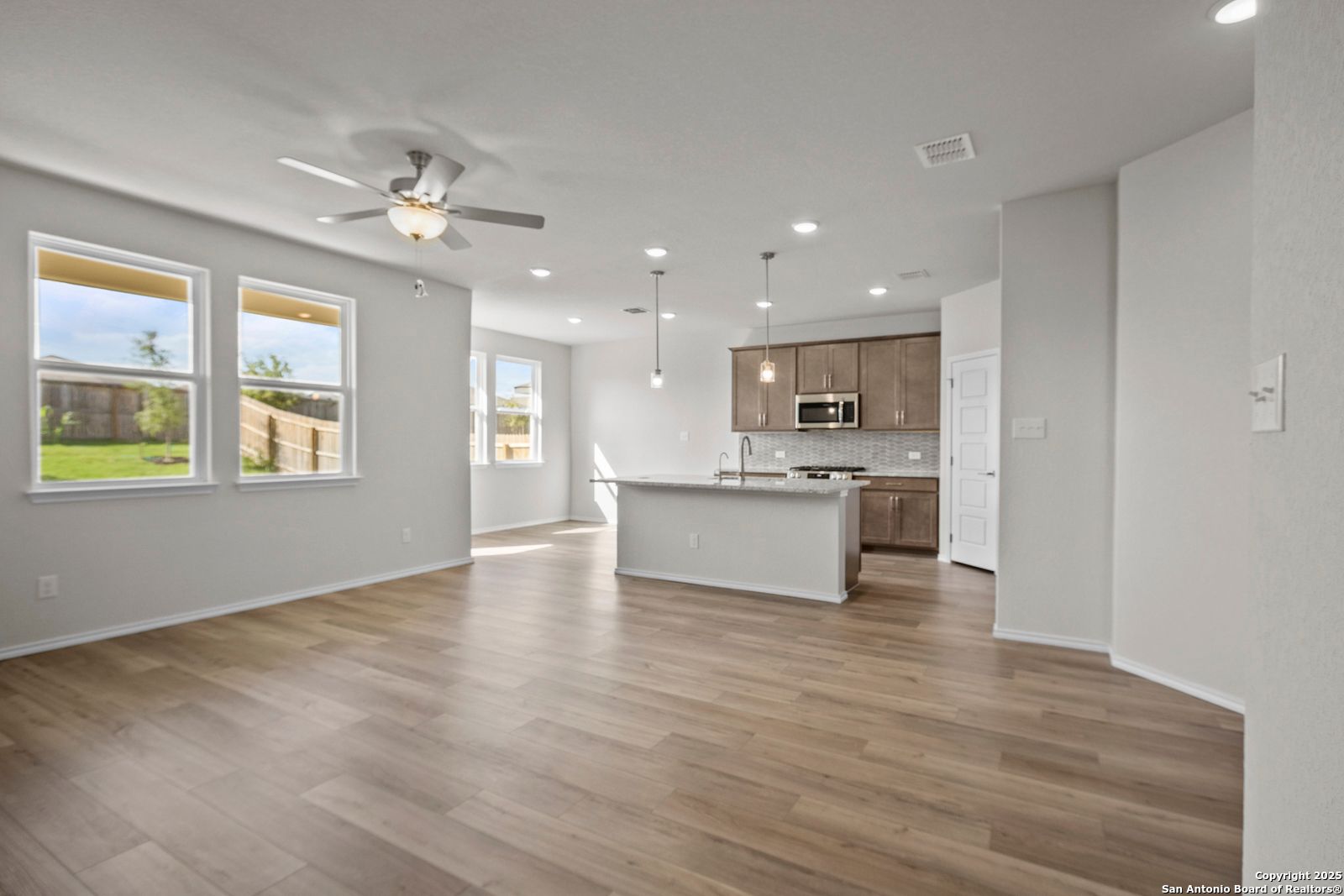 Modern open-concept kitchen with white island, wood floors, ceiling fan, and large windows in Davidson Homes Asheville J, San Antonio TX