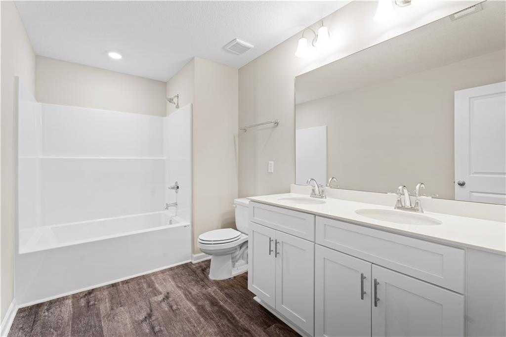 Modern bathroom with white bathtub, tiled shower, double vanity sinks, toilet, and wood flooring in Davidson Homes The Washington plan, Phenix City, Alabama
