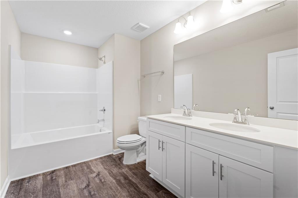 Modern bathroom with white bathtub, tiled shower, double vanity sinks, toilet, and wood flooring in Davidson Homes The Washington plan, Phenix City, Alabama