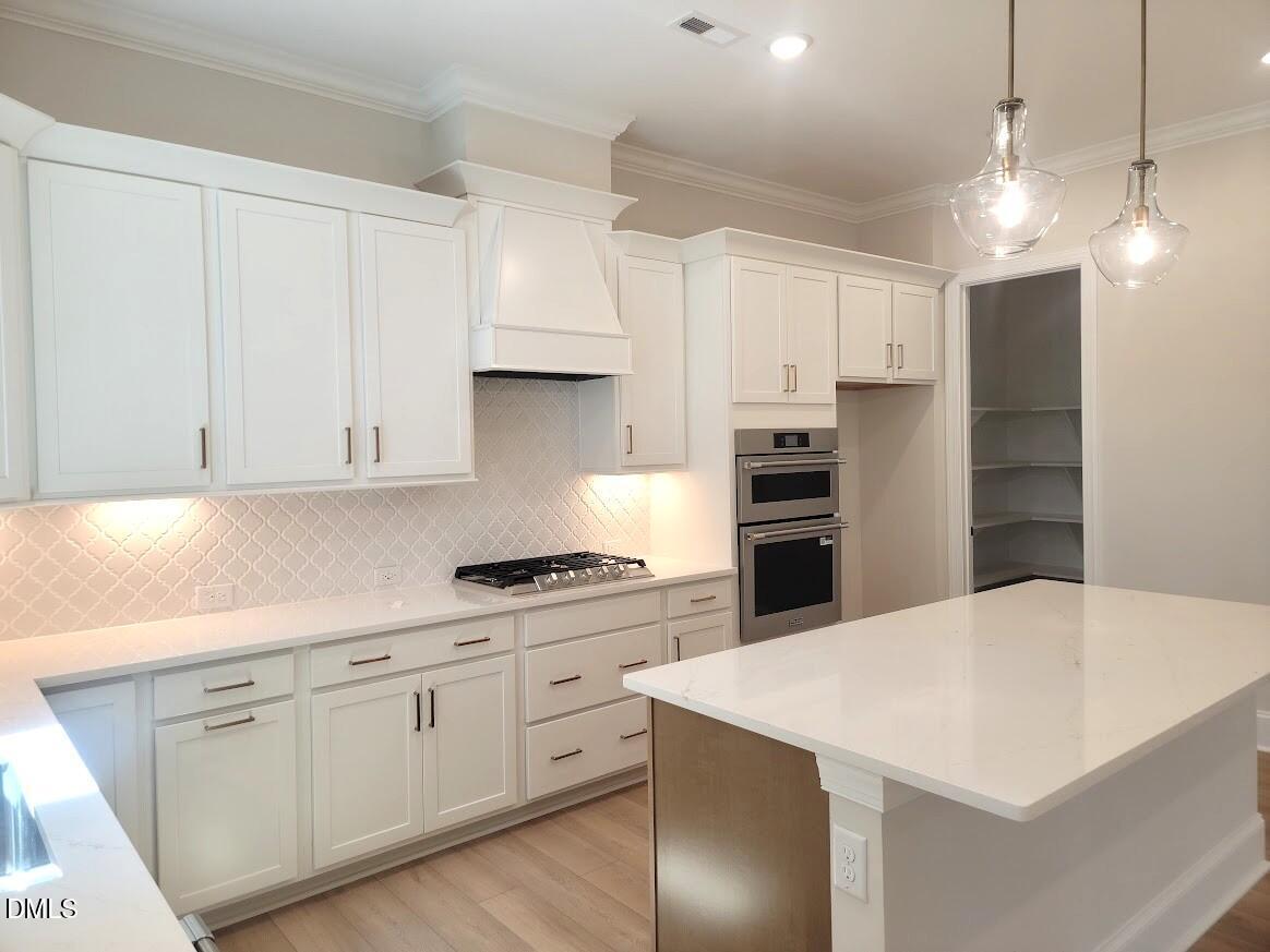 Bright white kitchen with quartz island, glass pendant lights, and built-in double ovens in The Crawford D, Wake Forest NC
