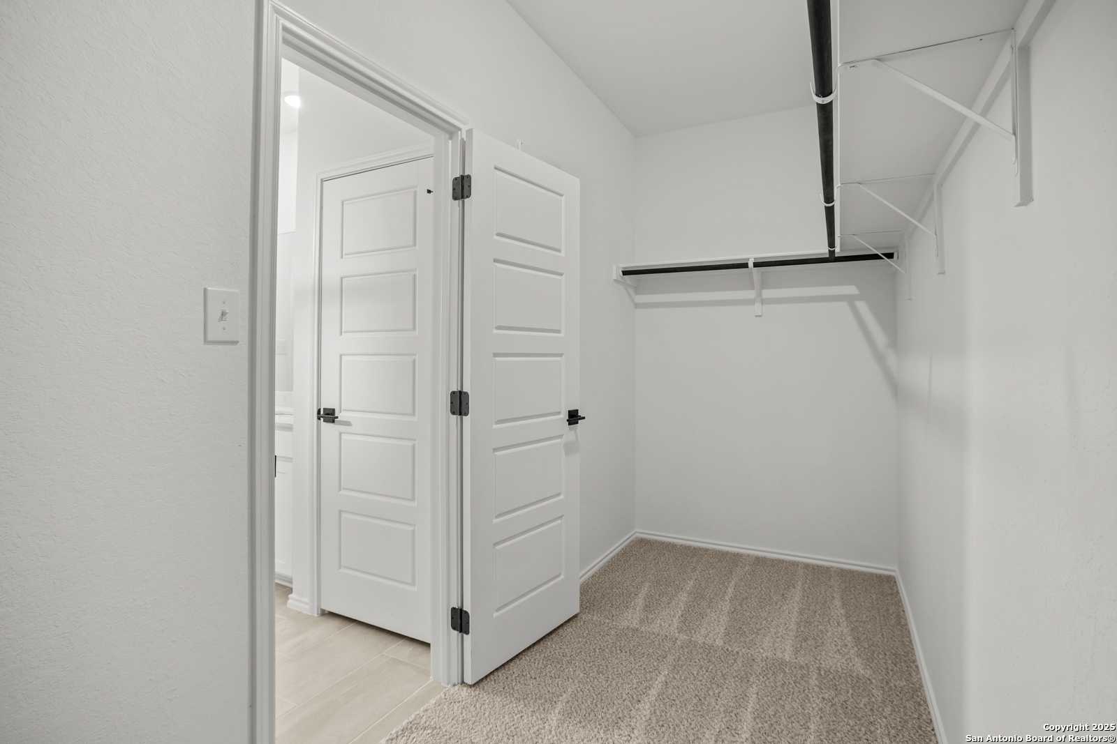 Spacious walk-in closet with double hanging rods, beige carpet, and adjacent bath door in Davidson Homes The Daphne K, San Antonio