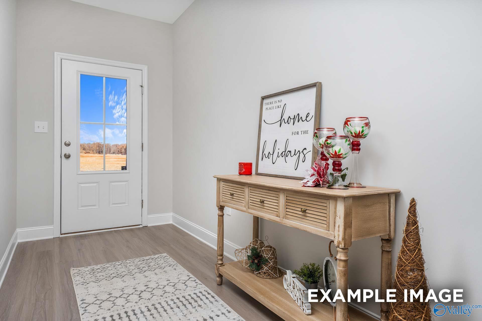 Festive entryway with wooden console table, "home for the holidays" sign, Christmas trees, and window view to countryside in The Daphne D, Meridianville, AL