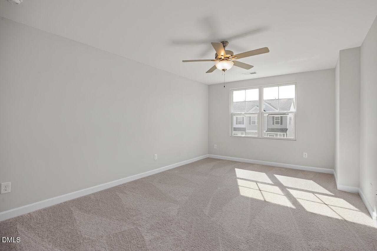Bright secondary bedroom with neutral walls, carpet floor, ceiling fan, and sunny windows in Davidson Homes The Warren, Fuquay-Varina, NC