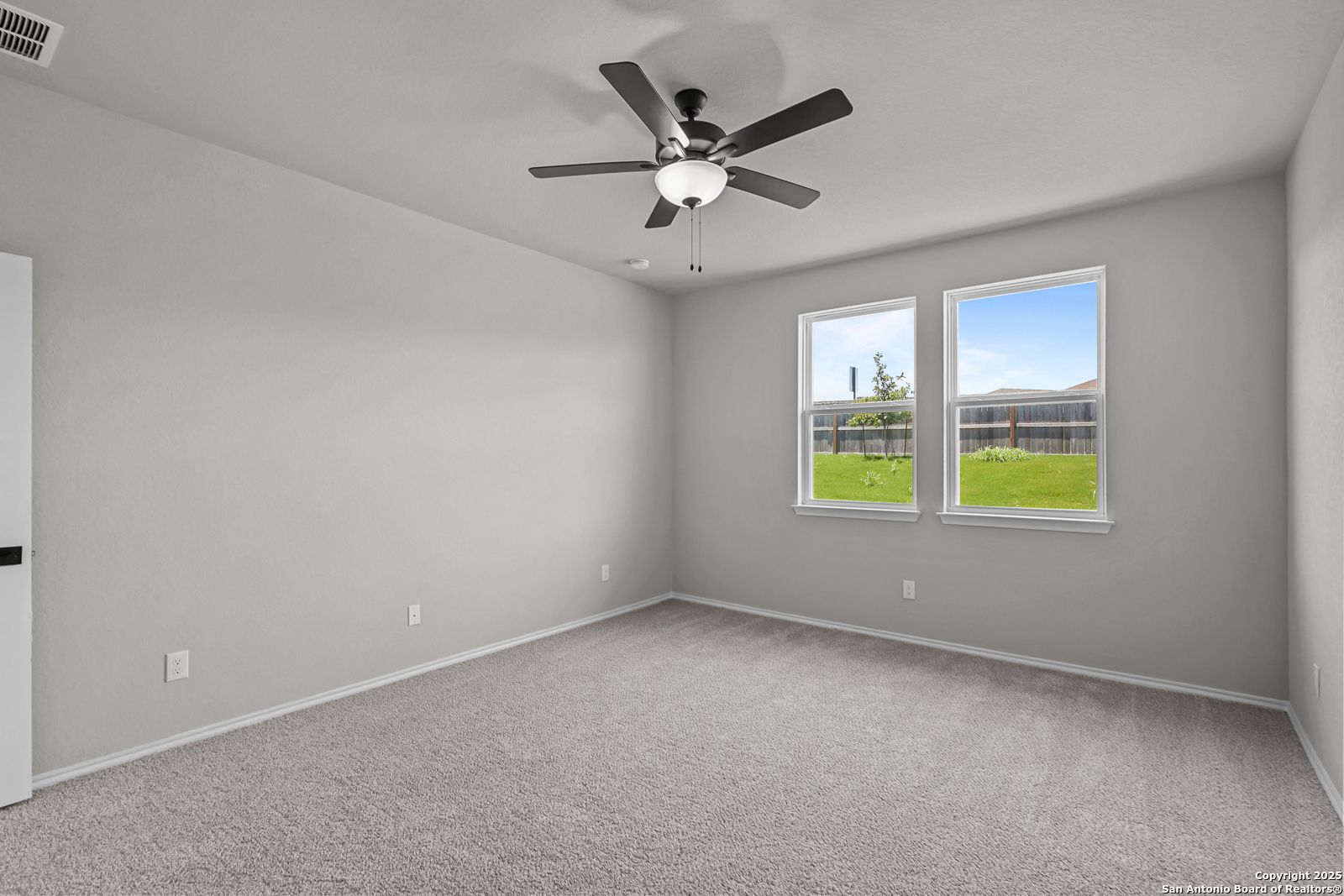 Bright bedroom with gray walls, ceiling fan, carpet floor, and windows overlooking green lawn in Davidson Homes The Daphne K, San Antonio