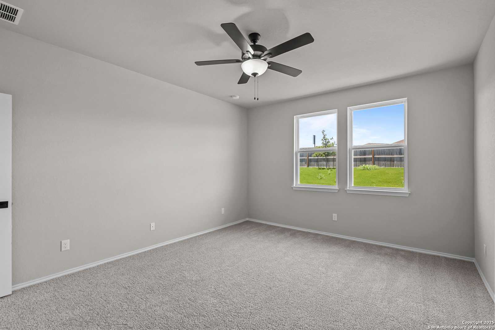 Bright empty secondary bedroom with ceiling fan, gray walls, and windows overlooking green lawn in Davidson Homes The Daphne K, San Antonio