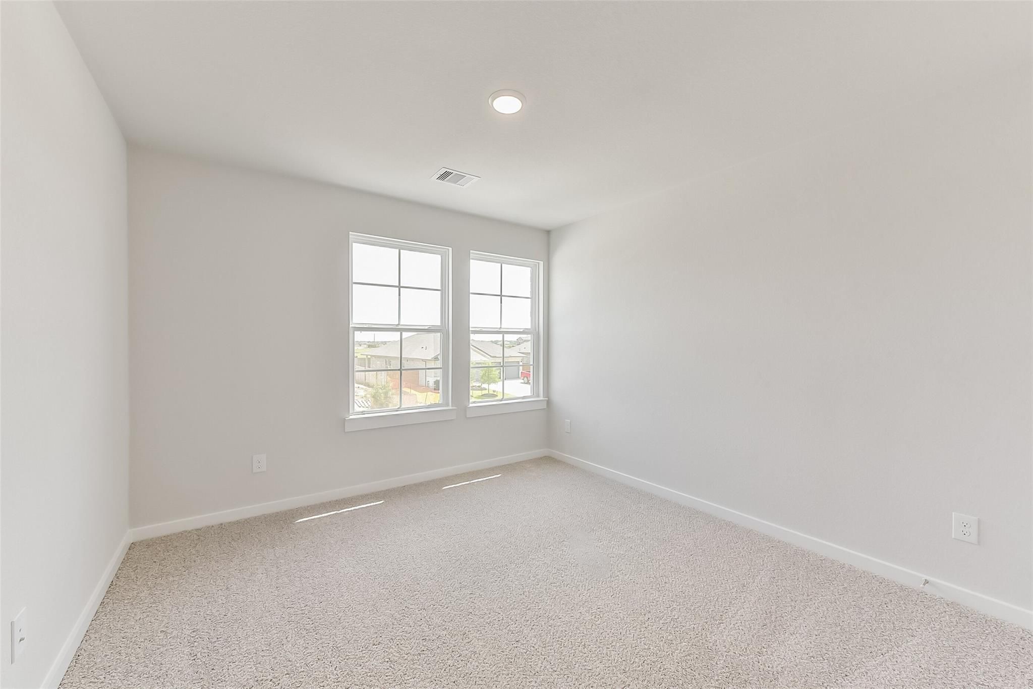 Bright empty secondary bedroom with large windows, beige carpet, and neutral walls in Davidson Homes The Tierra C, Dayton, Texas