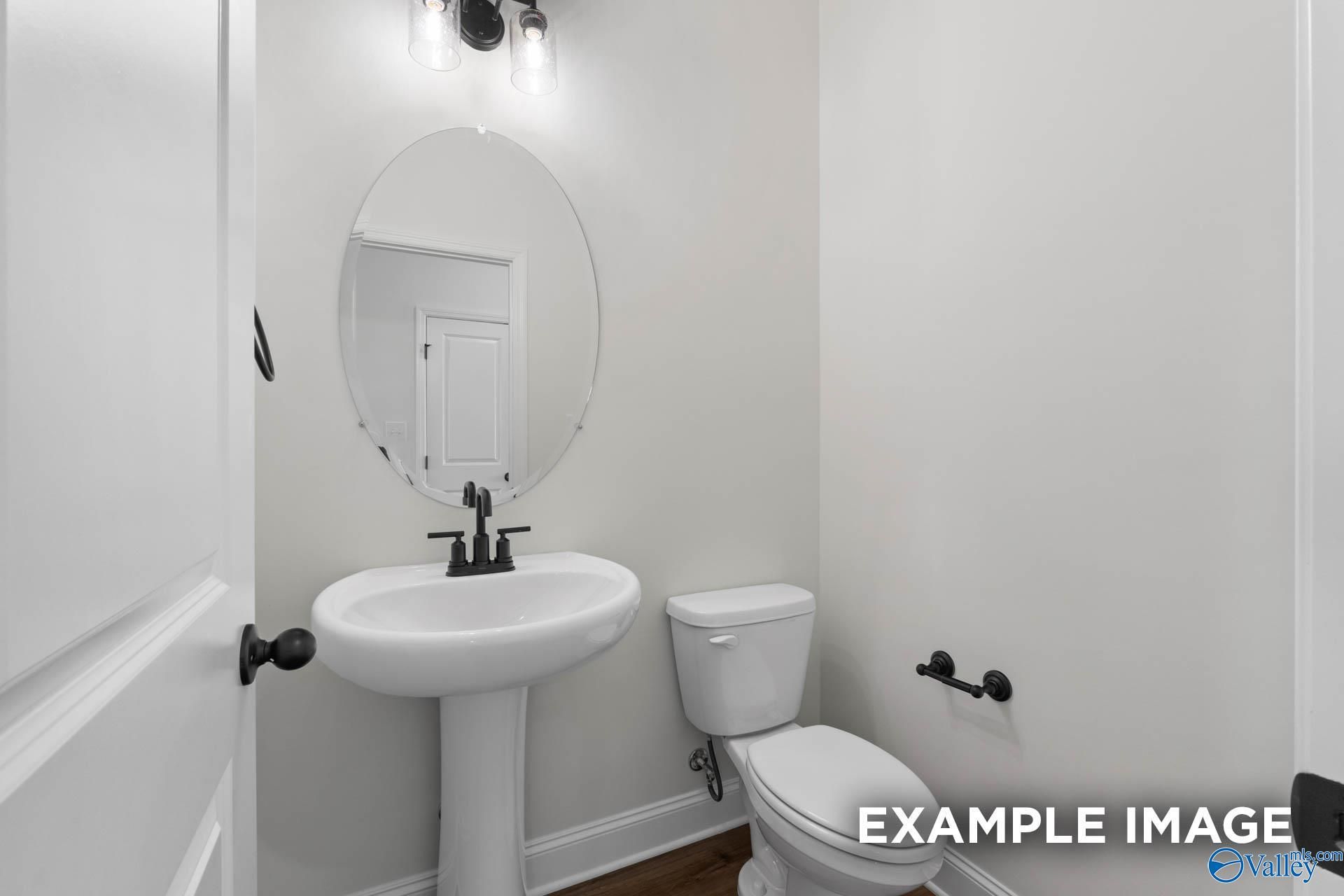 Half bathroom with pedestal sink, oval mirror, and matte black fixtures in The Rockford B plan, Briercreek, Meridianville.