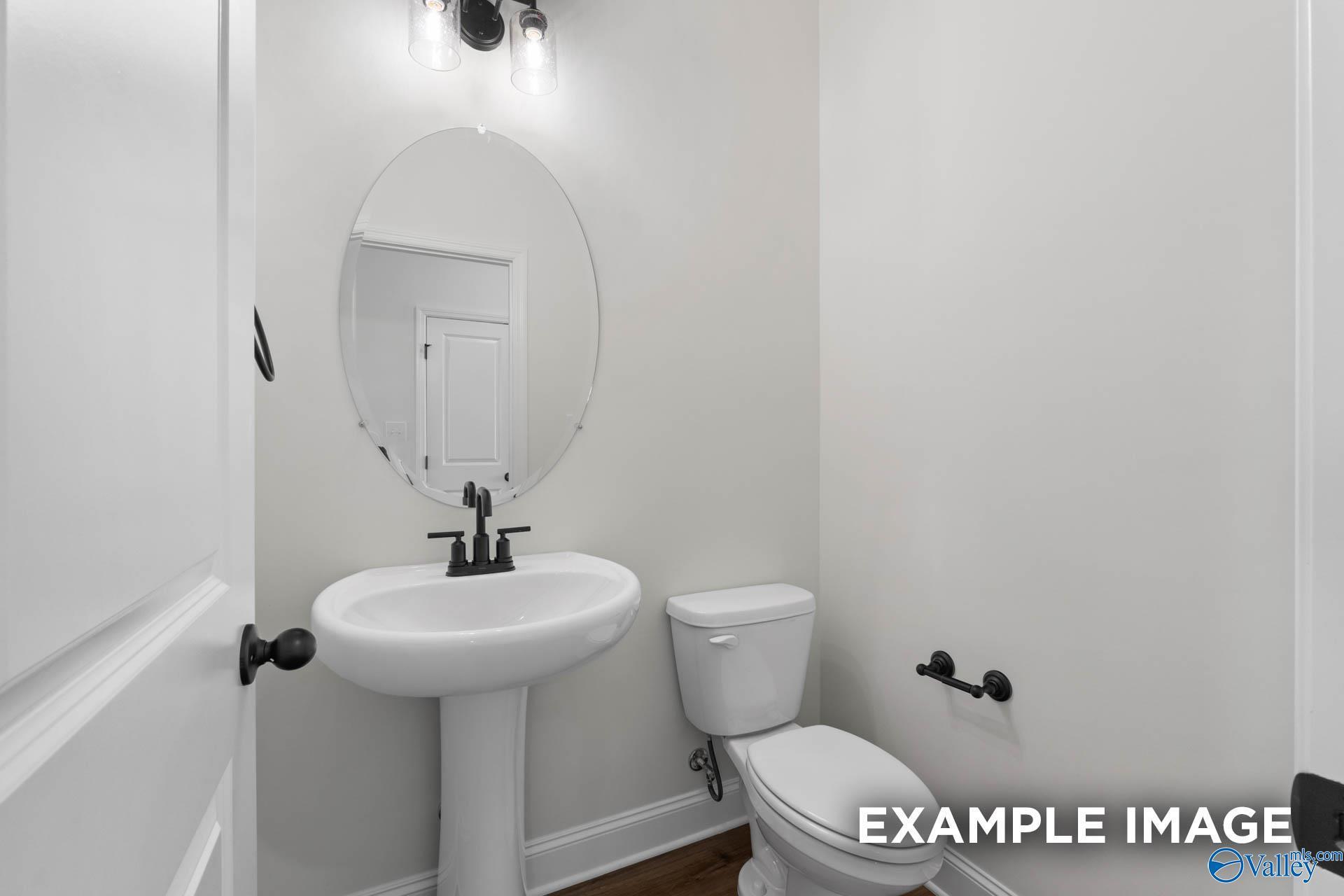 Half bathroom with pedestal sink, oval mirror, and matte black fixtures in The Rockford B plan, Briercreek, Meridianville.