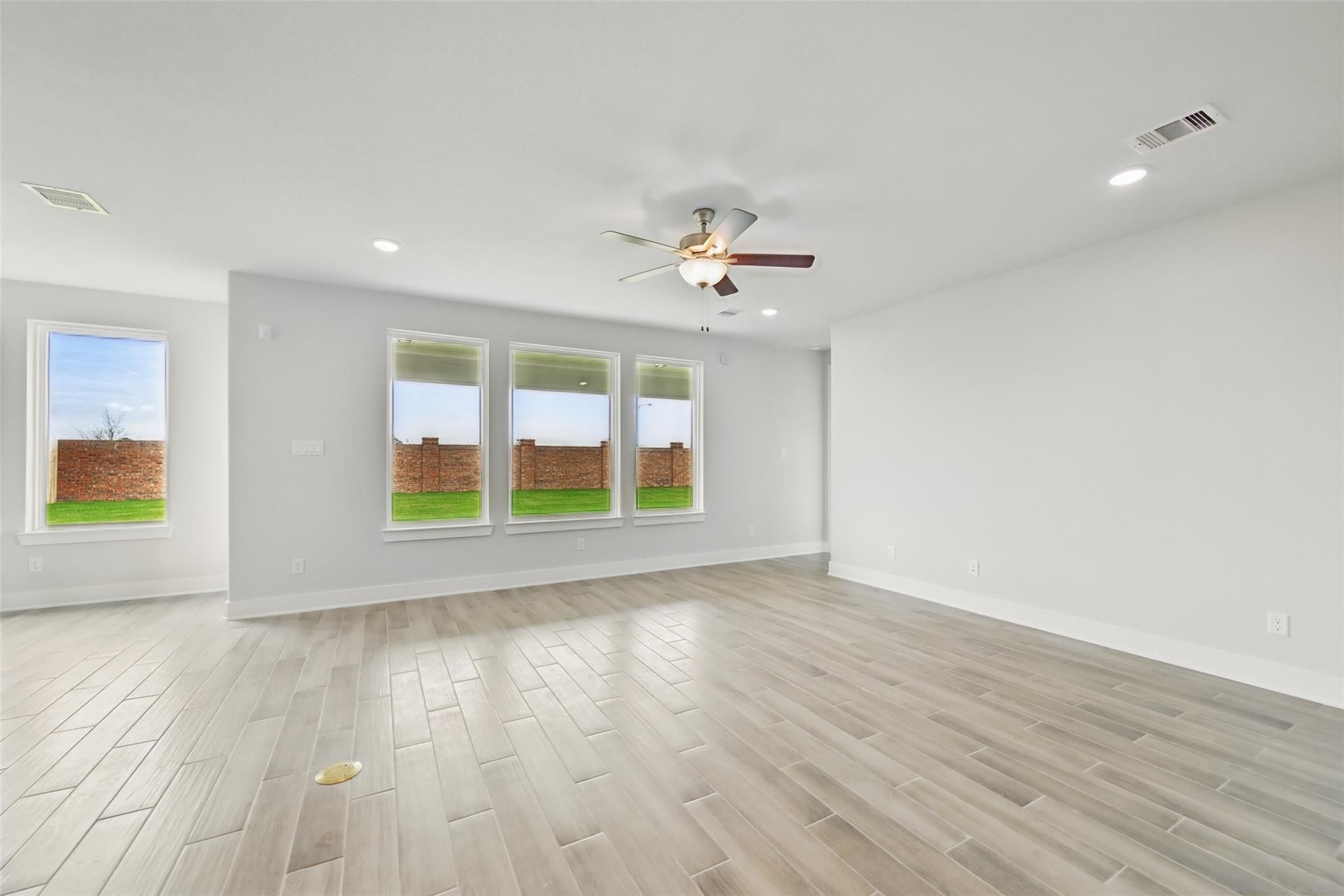 Spacious living room with ceiling fan, large windows overlooking green backyard, light wood floors in Davidson Homes The Philip A, Lago Mar