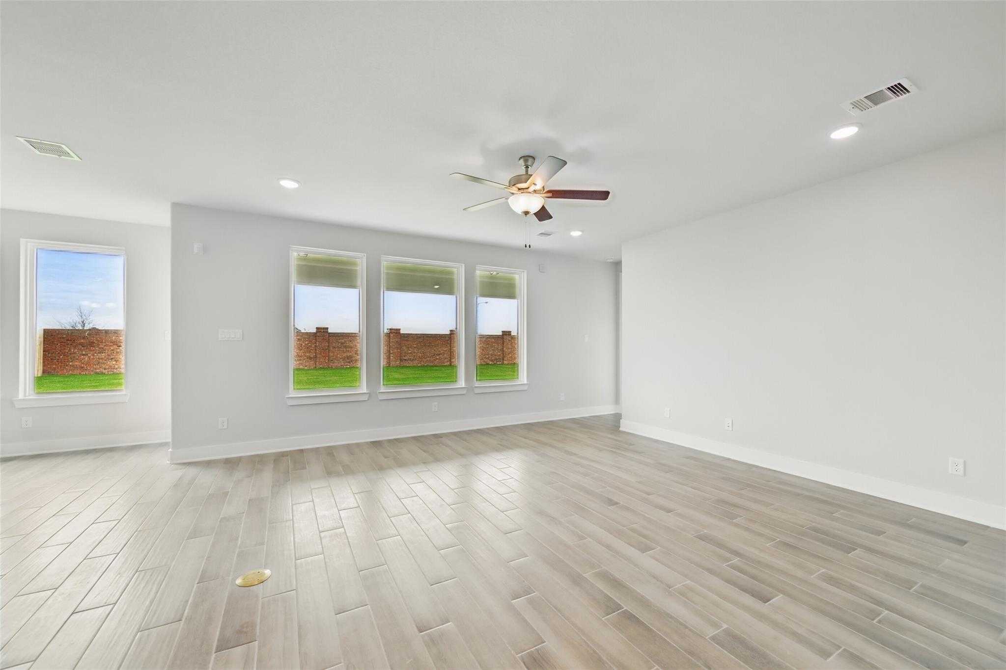 Spacious living room with ceiling fan, large windows to green backyard, light wood floors in 4-bedroom The Philip A home, Lago Mar, Texas City