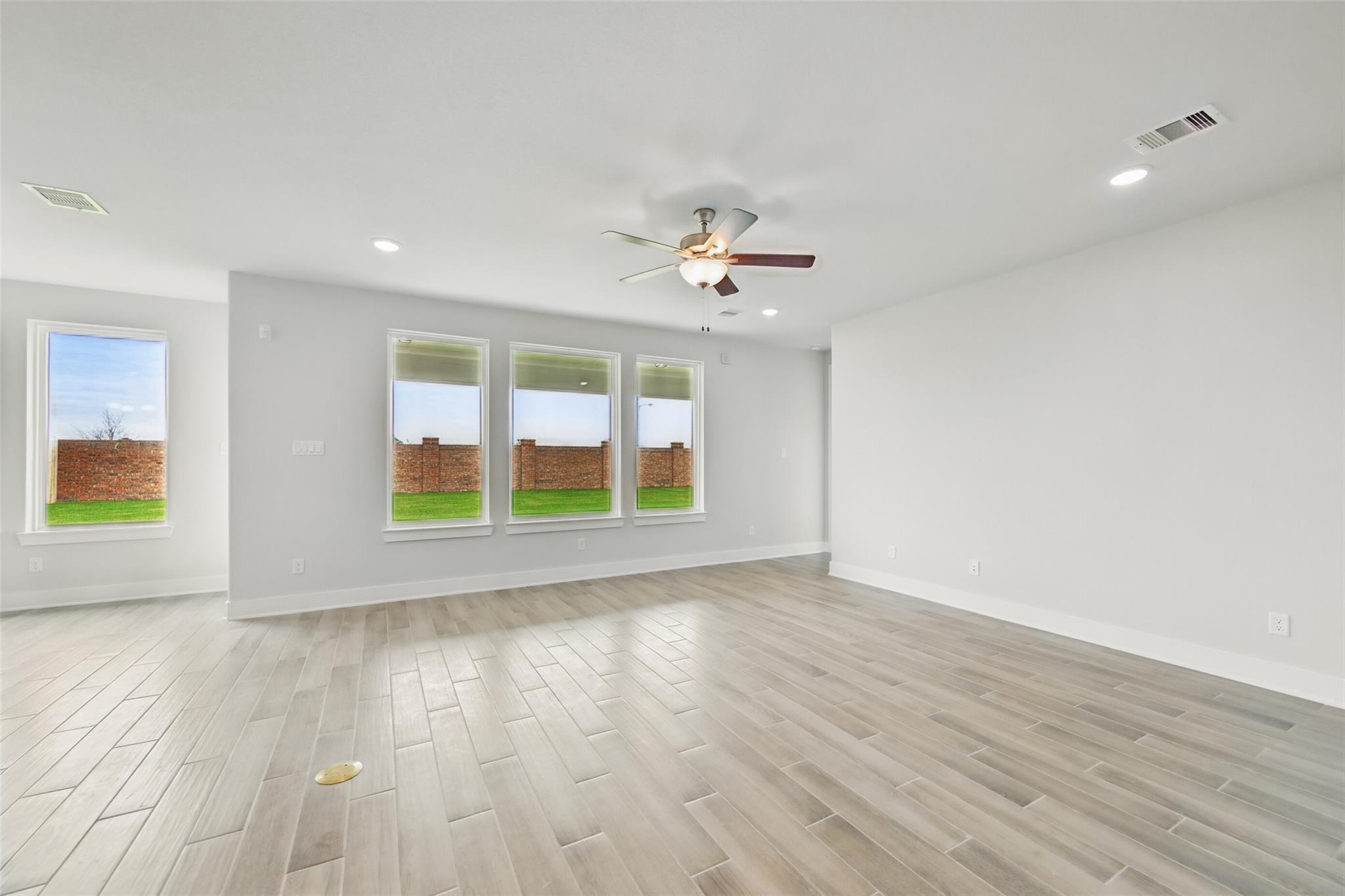 Spacious living room with ceiling fan, large windows overlooking green backyard, light wood floors in Davidson Homes The Philip A, Lago Mar