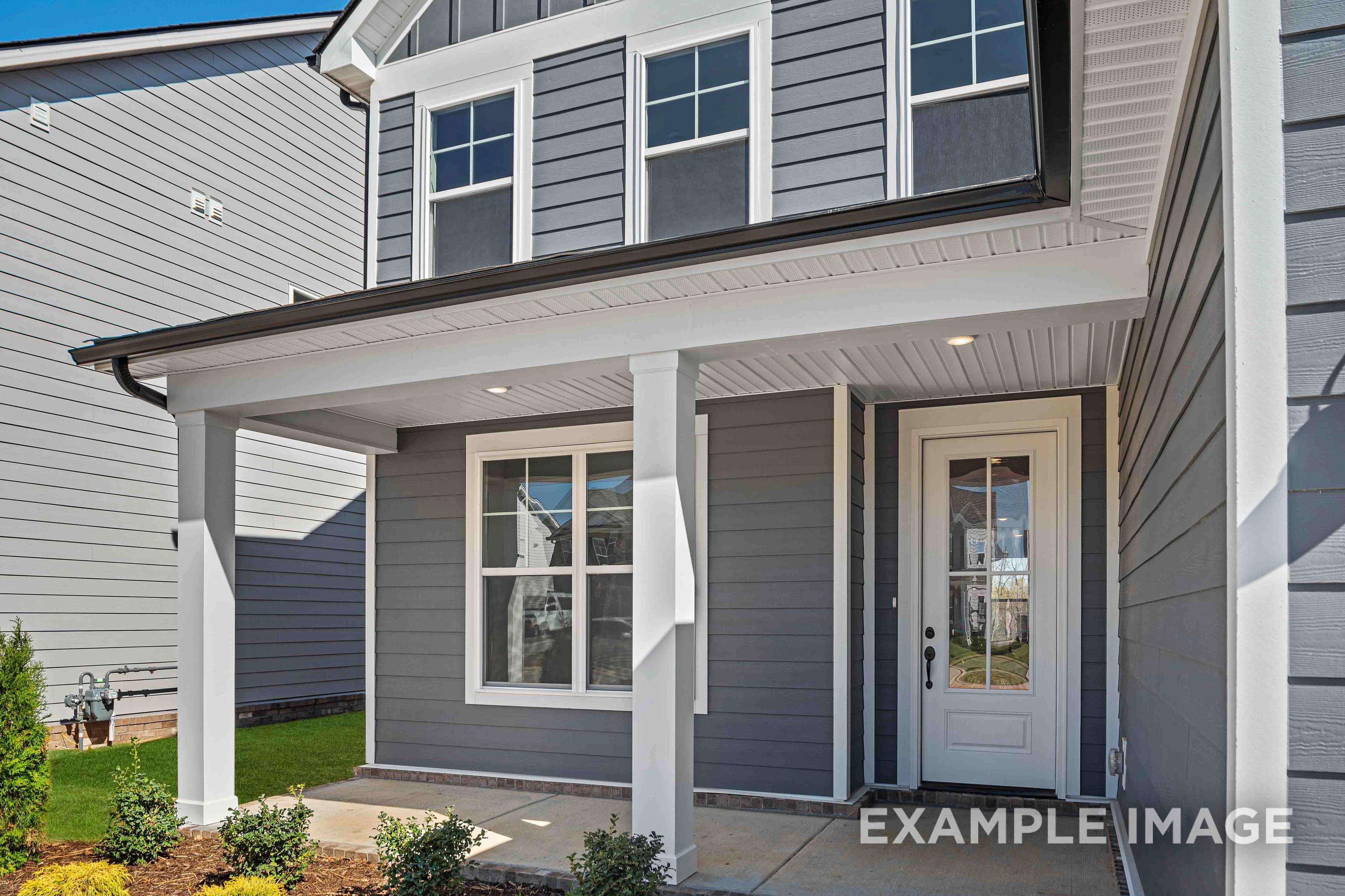 Two-story The Ash home elevation featuring gray siding, covered front porch with white columns, and glass-paneled door in Mt. Juliet