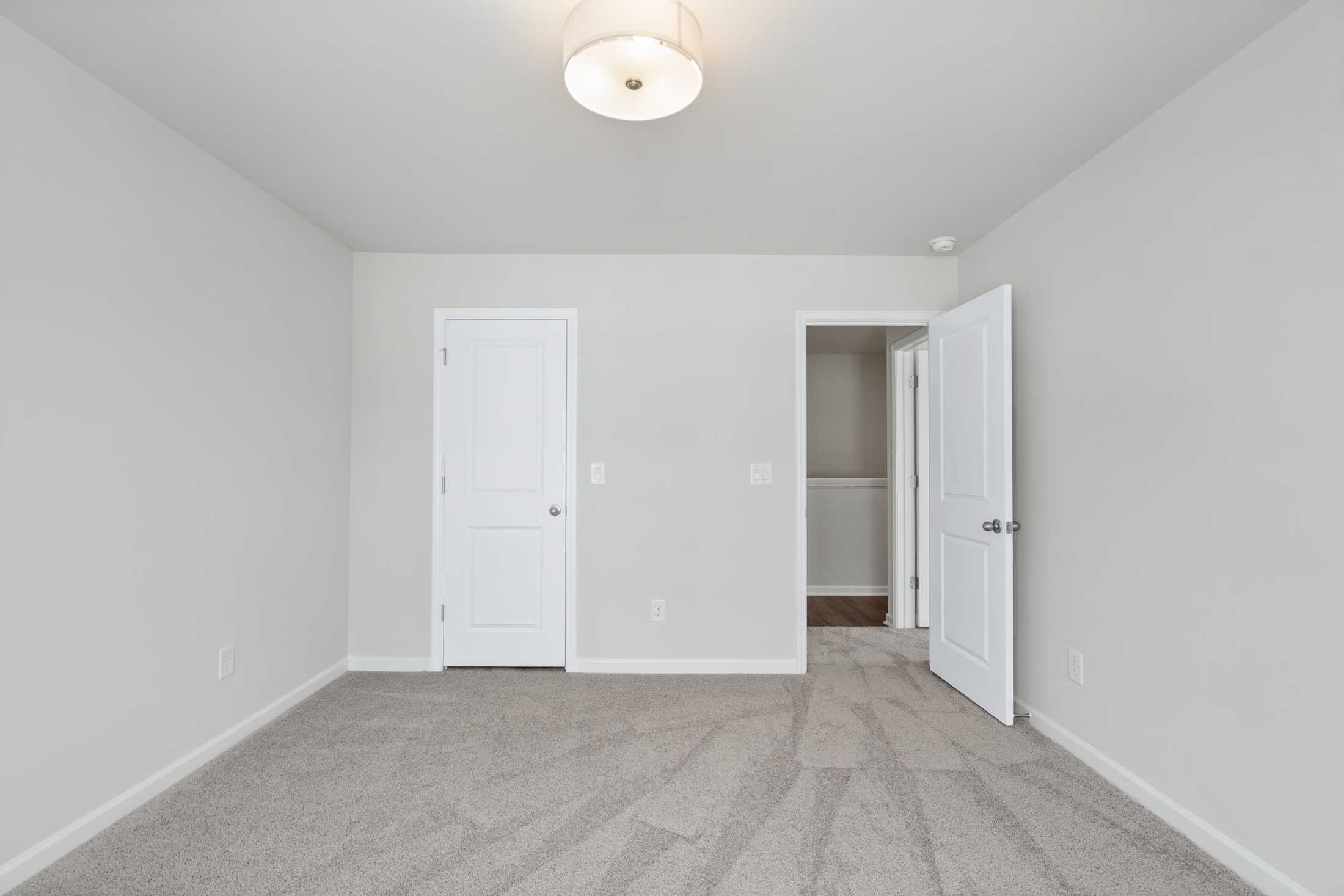 Spacious master bedroom in The Cary A by Davidson Homes, featuring light gray walls, beige carpet, white doors, and ceiling light in Winder GA