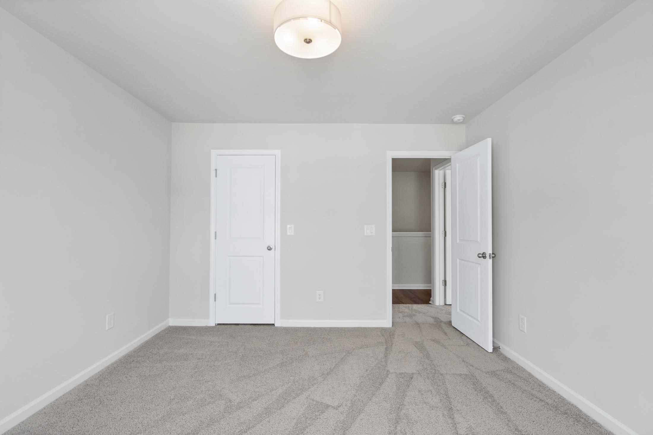 Spacious master bedroom in The Cary A by Davidson Homes, featuring light gray walls, beige carpet, white doors, and ceiling light in Winder GA