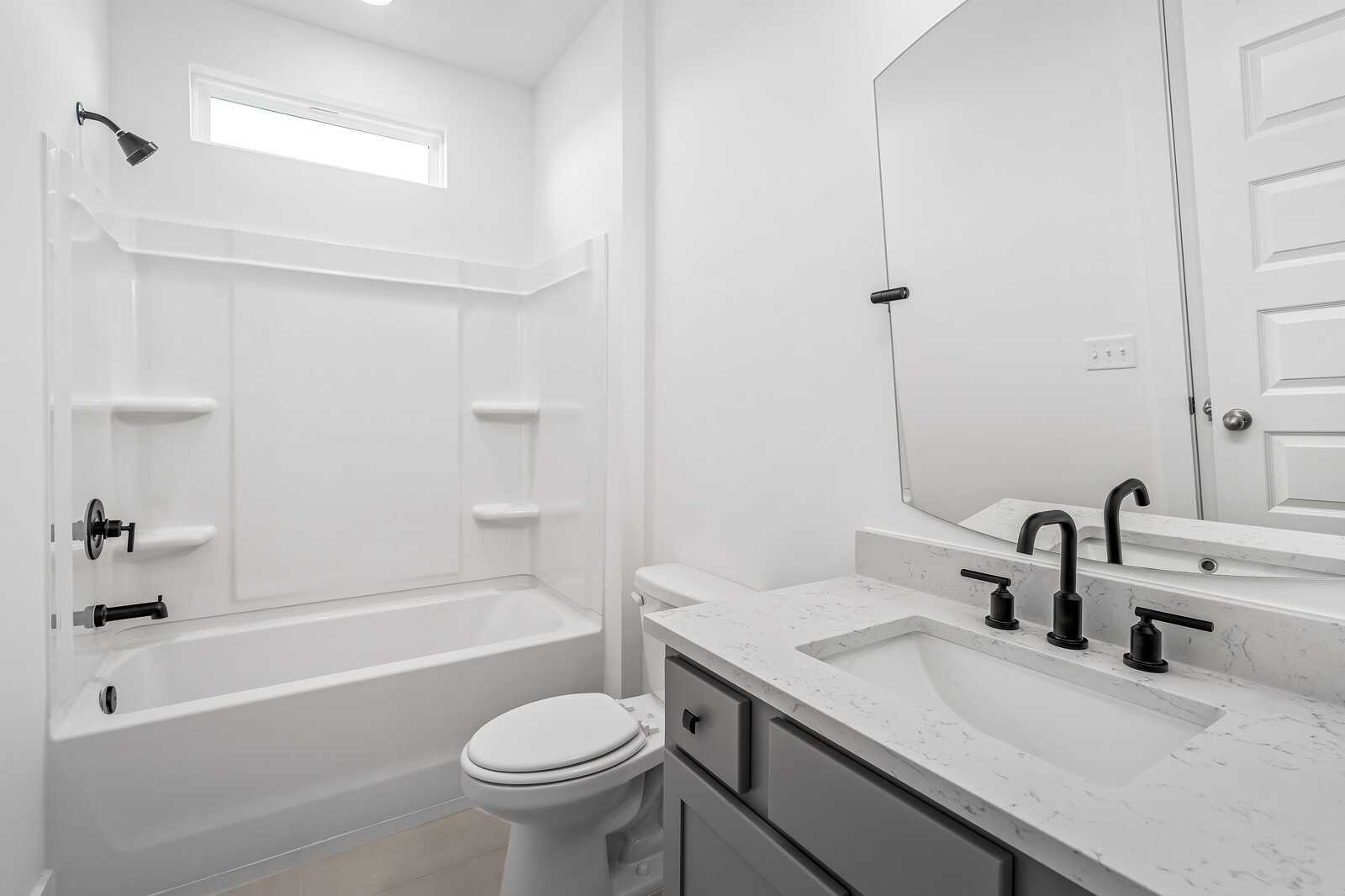 Modern guest bathroom featuring white subway tile tub-shower combo, gray vanity with quartz countertop, and round mirror in Davidson Homes The Alston A, Murfreesboro, TN