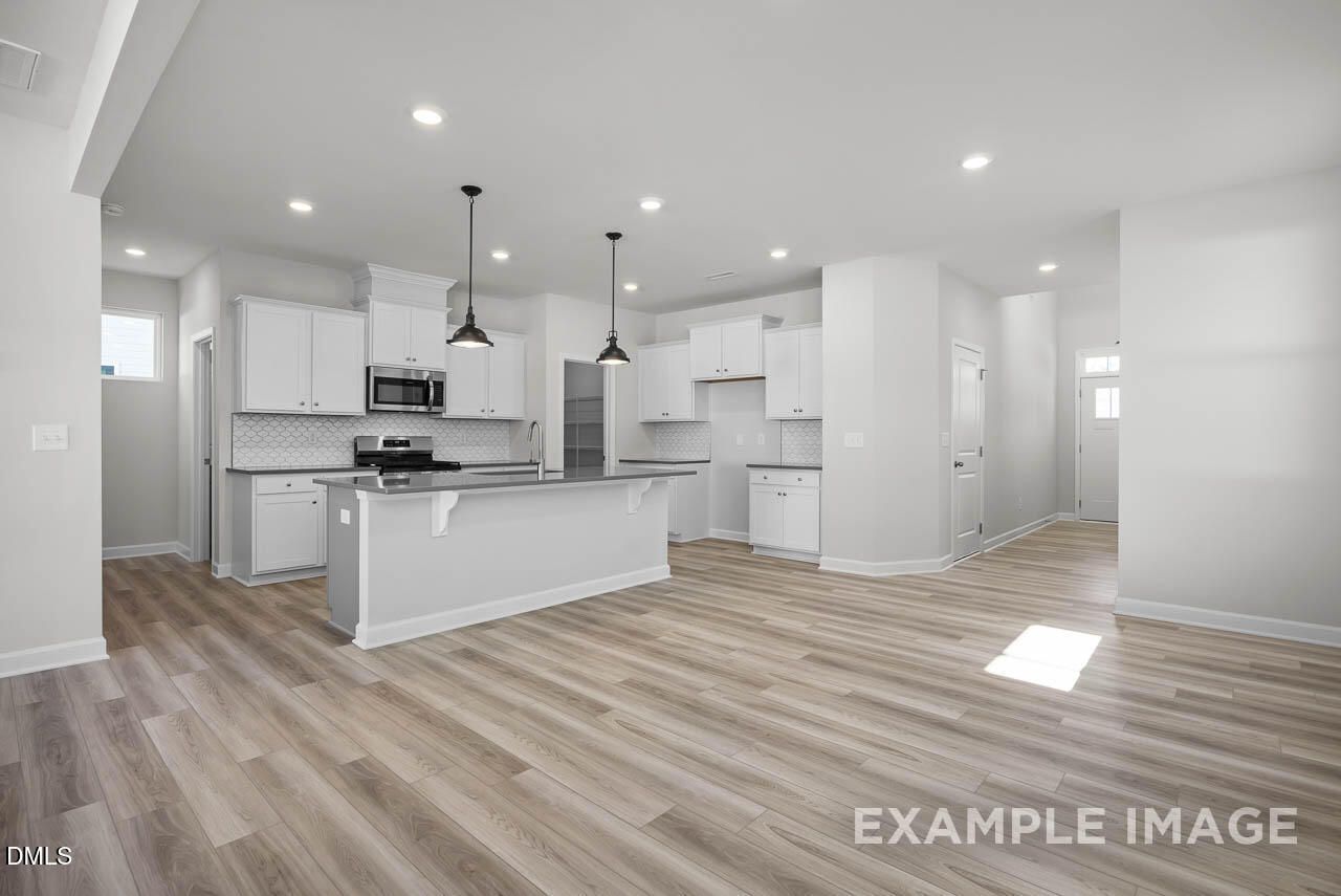 Open-concept kitchen with white cabinets, large island, pendant lights, and hardwood floors in Davidson Homes The Adalynn A, Lillington, NC
