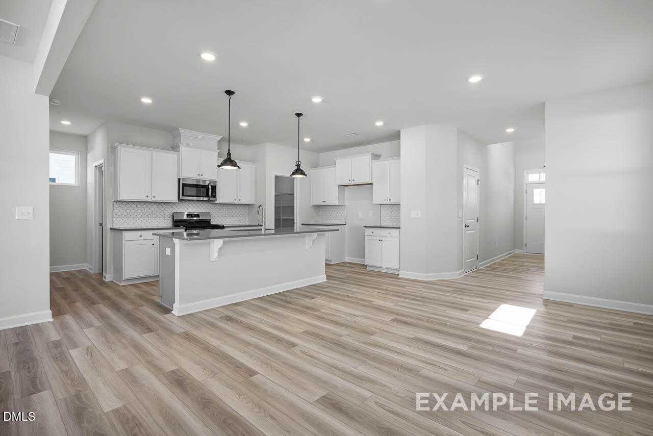 Open-concept kitchen with white cabinets, large island, pendant lights, and hardwood floors in Davidson Homes The Adalynn A, Lillington, NC