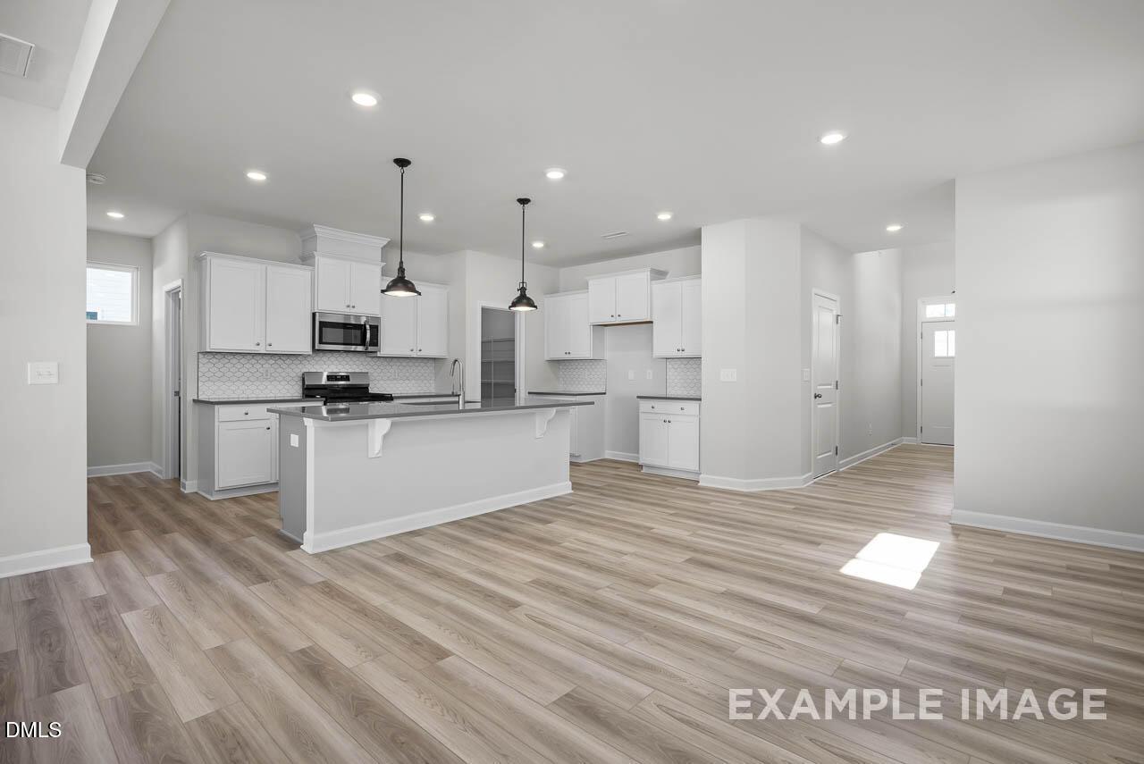 Spacious open-concept kitchen with white cabinets, island, stainless appliances, and pendant lights in Davidson Homes The Adalynn A, Lillington, NC