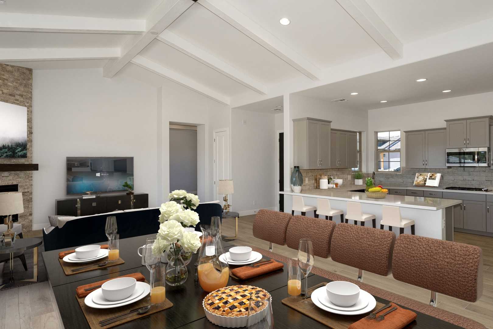 Open-concept living and dining in The Daybreak C by Davidson Homes: stone fireplace, set table, modern kitchen island, vaulted ceiling