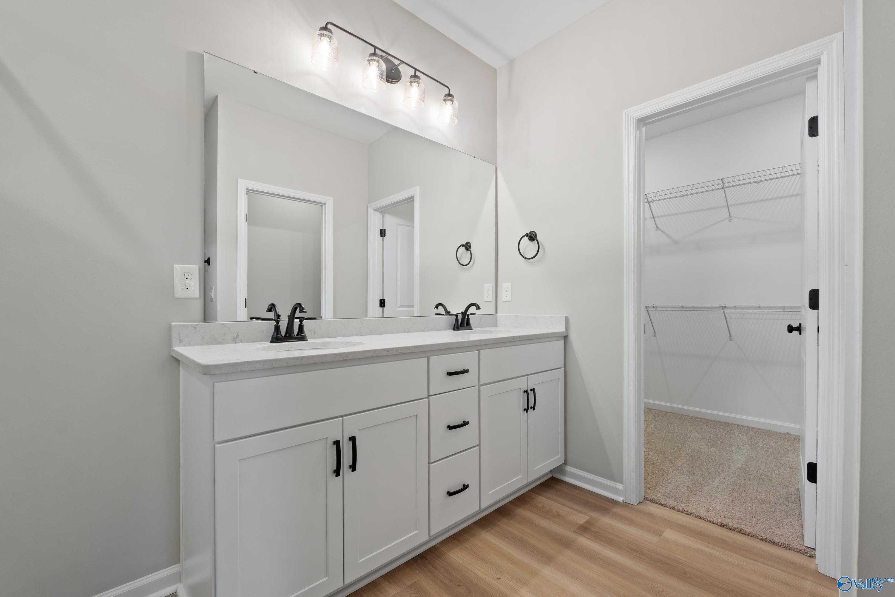 Modern double vanity with white shaker cabinets, framed mirror, and adjacent walk-in closet in The Nantucket by Evermore Homes, Madison, AL