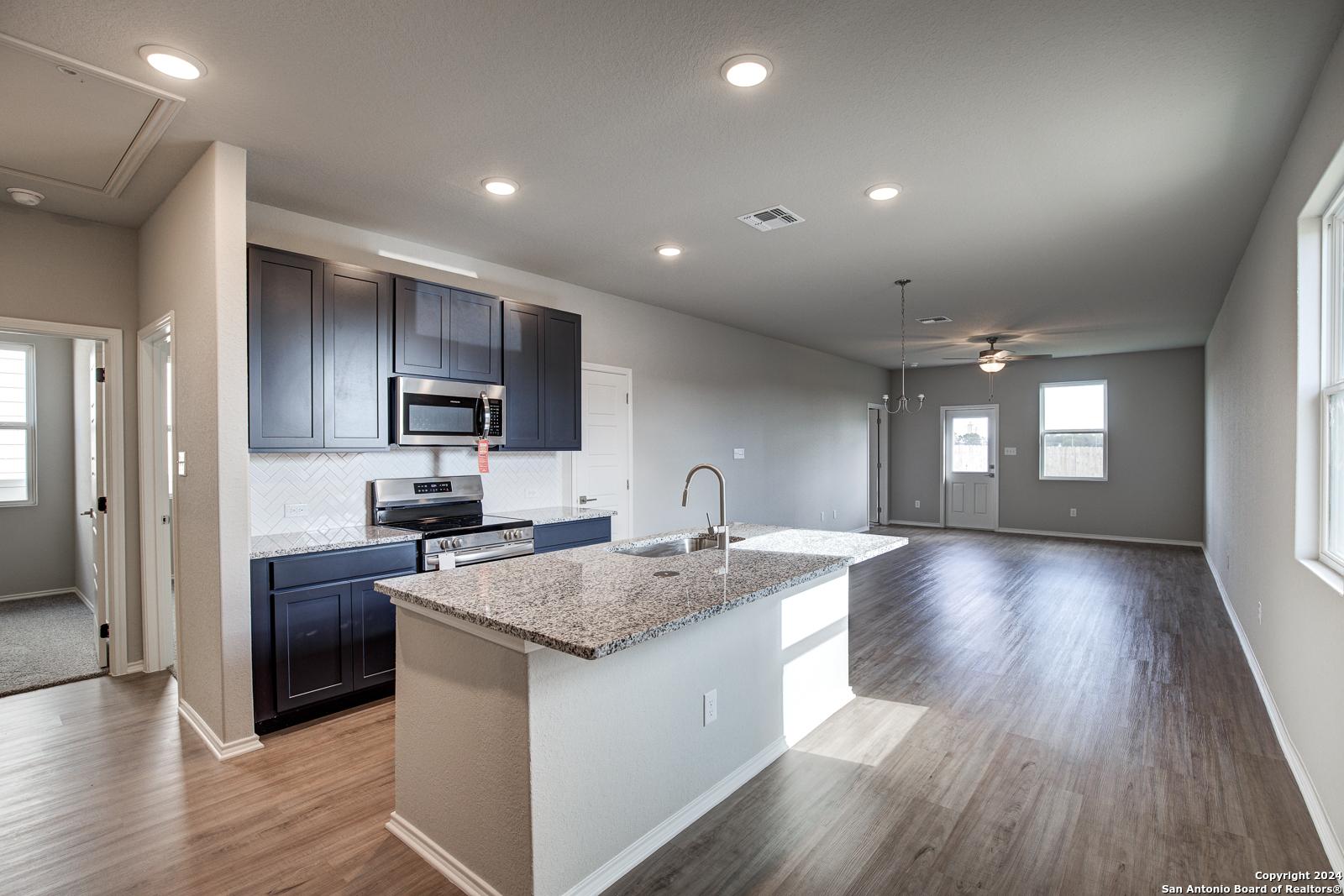 Spacious open-concept kitchen with dark cabinets, granite island, and stainless microwave in Davidson Homes The Frio B, San Antonio