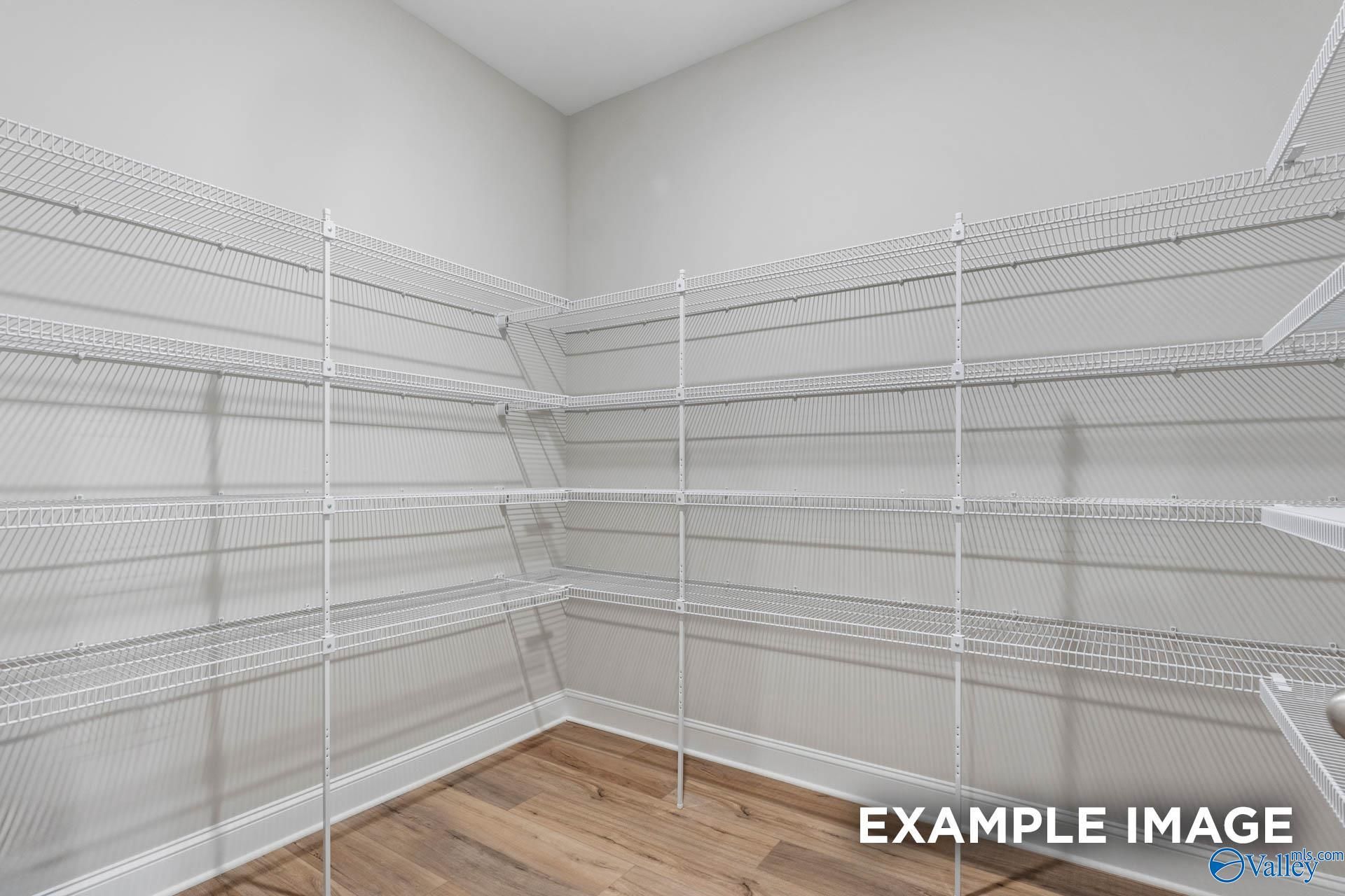 Spacious walk-in pantry with white wire shelving on gray walls and hardwood floors in The Finleigh home, Creekside, Harvest, AL