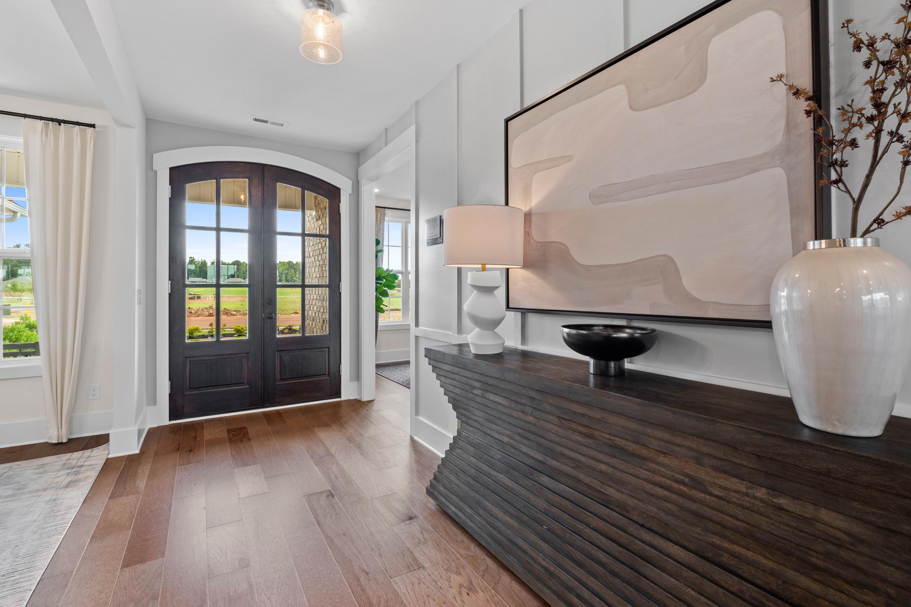 Elegant Creekside foyer in Harvest Alabama featuring arched dark wood door, hardwood floors, abstract art, and console table