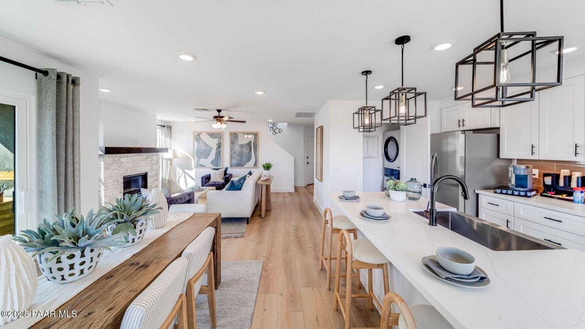 Open-concept kitchen and living room with white cabinets, stainless appliances, wooden island, and stone fireplace in Davidson Homes The Wilmington B, Prescott AZ