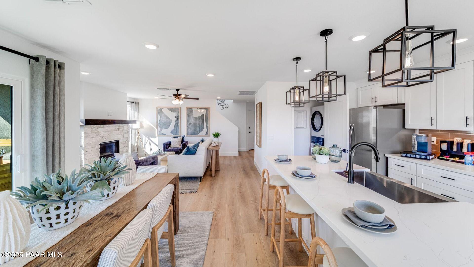 Open-concept kitchen and living room with white cabinets, stainless appliances, wooden island, and stone fireplace in Davidson Homes The Wilmington B, Prescott AZ