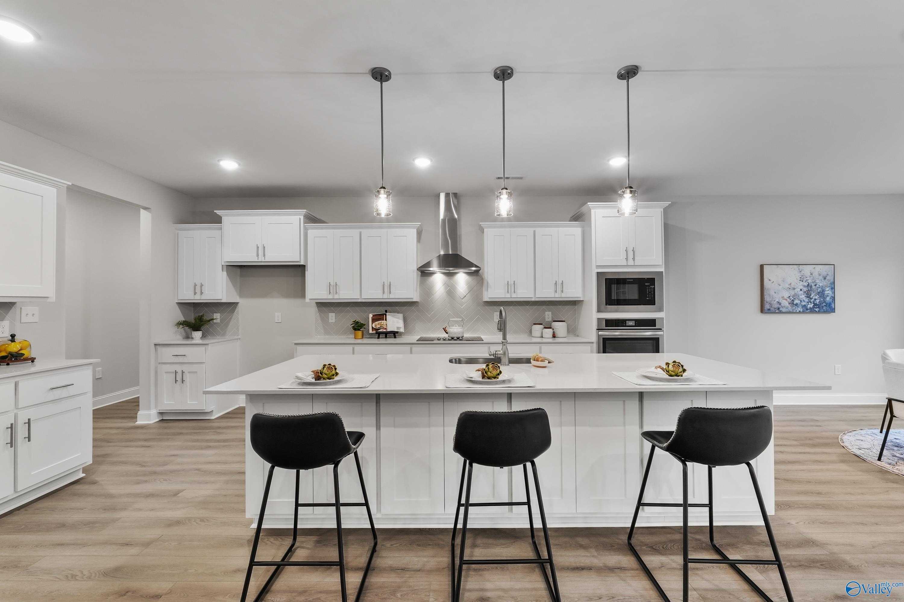 Modern open-concept kitchen with white island, stainless steel appliances, pendant lights in The Finleigh by Davidson Homes, Toney, AL