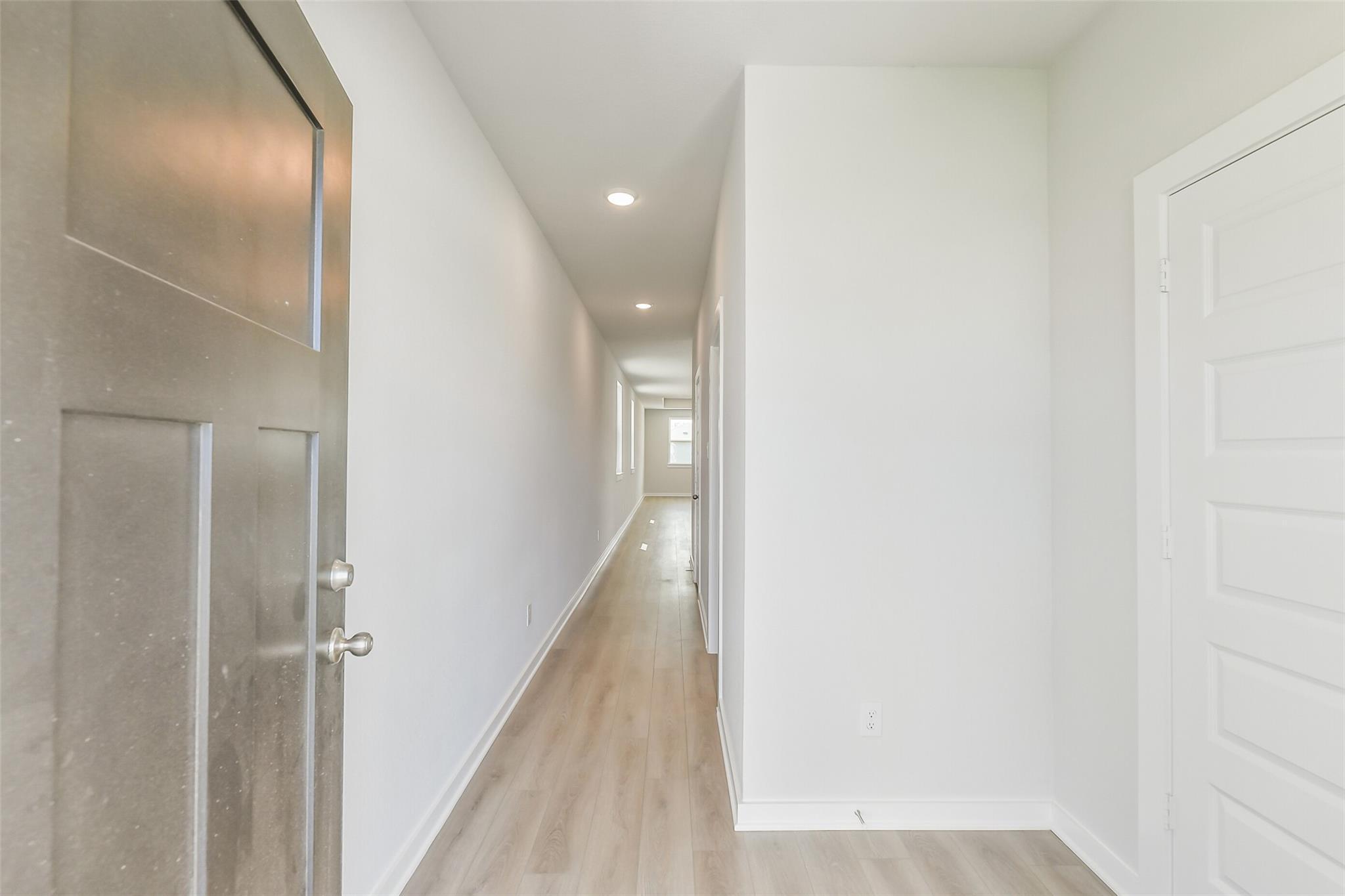 Bright hallway with white walls, recessed lights, and light oak flooring in Davidson Homes The Frio G, Conroe Texas